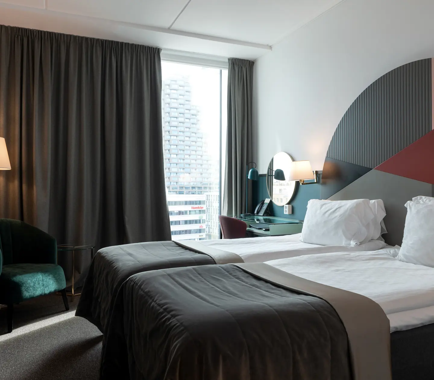 Ljust hotellrum med sängar, färgglad sänggavel och fönster