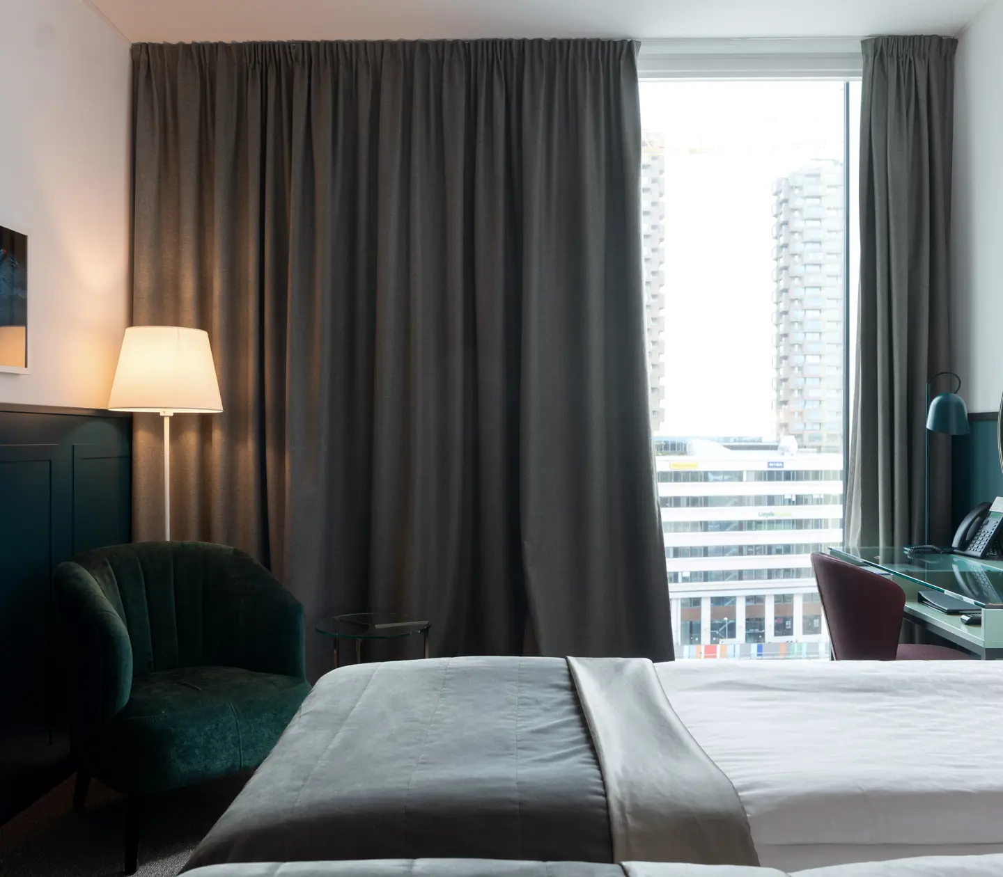 Ljust hotellrum med sängar, skrivbord och stort fönster