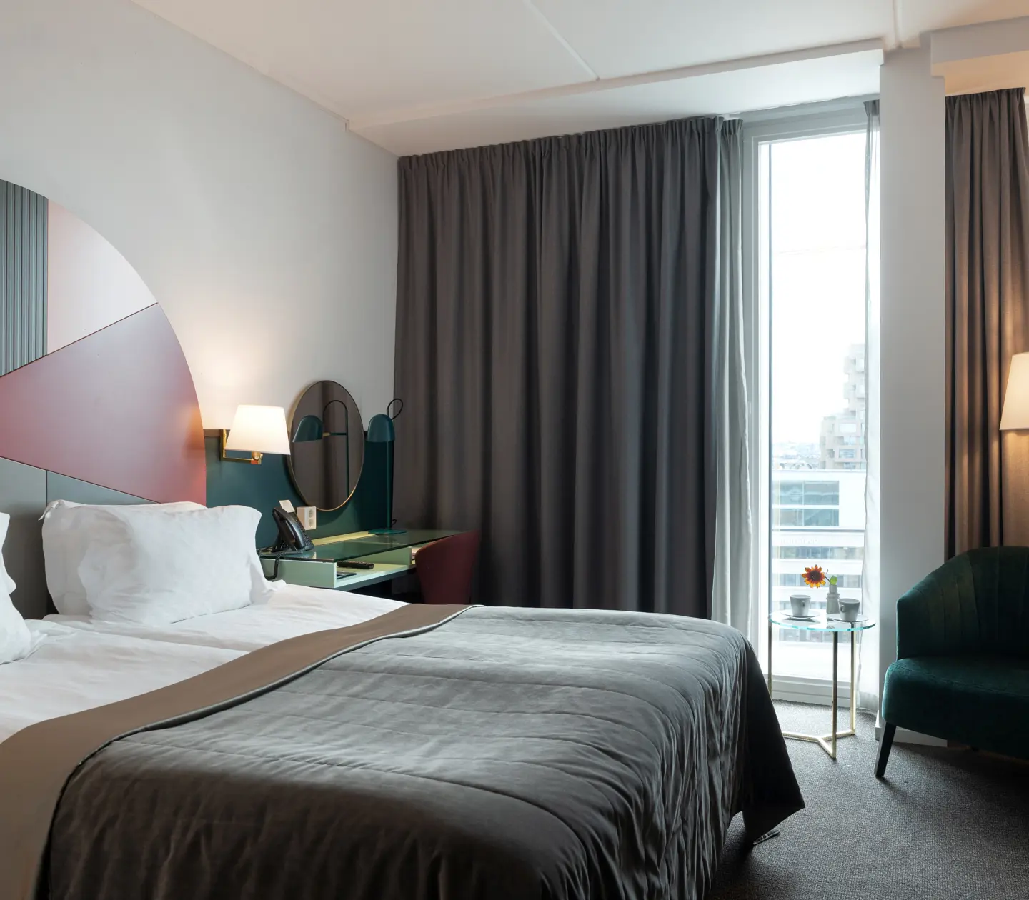 Ljust hotellrum med säng, färgglad sänggavel och fönster