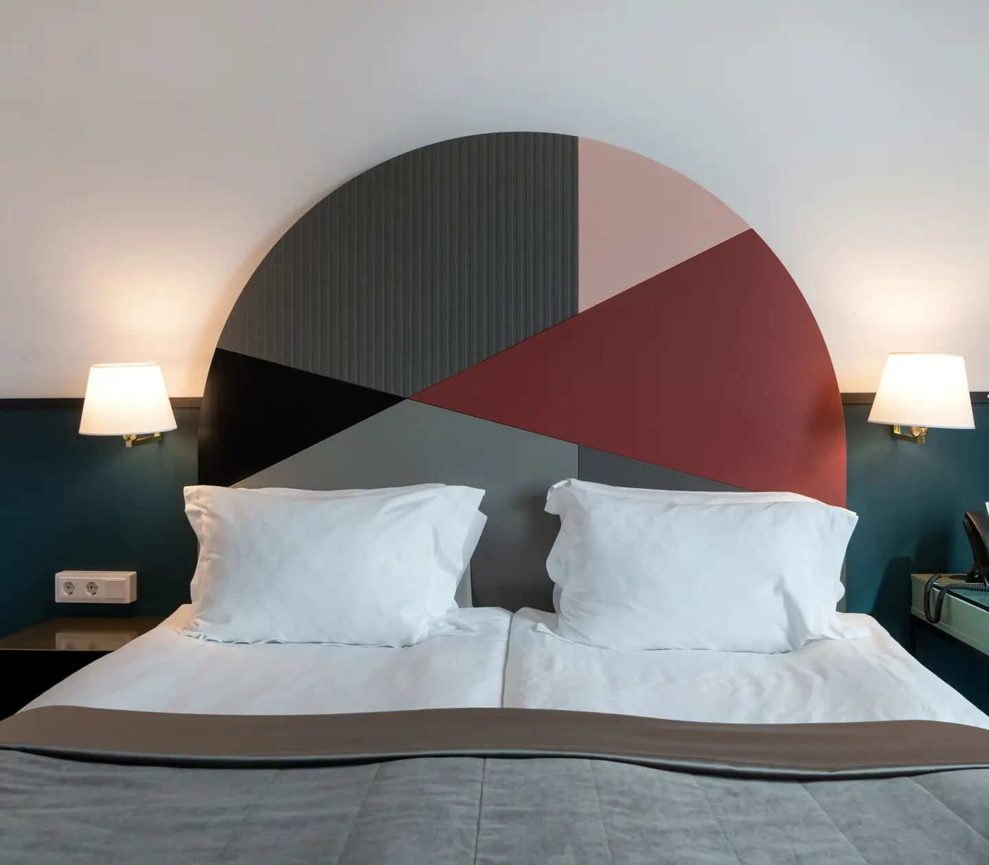 Ljust hotellrum med säng, färgglad sänggavel och sänglampa