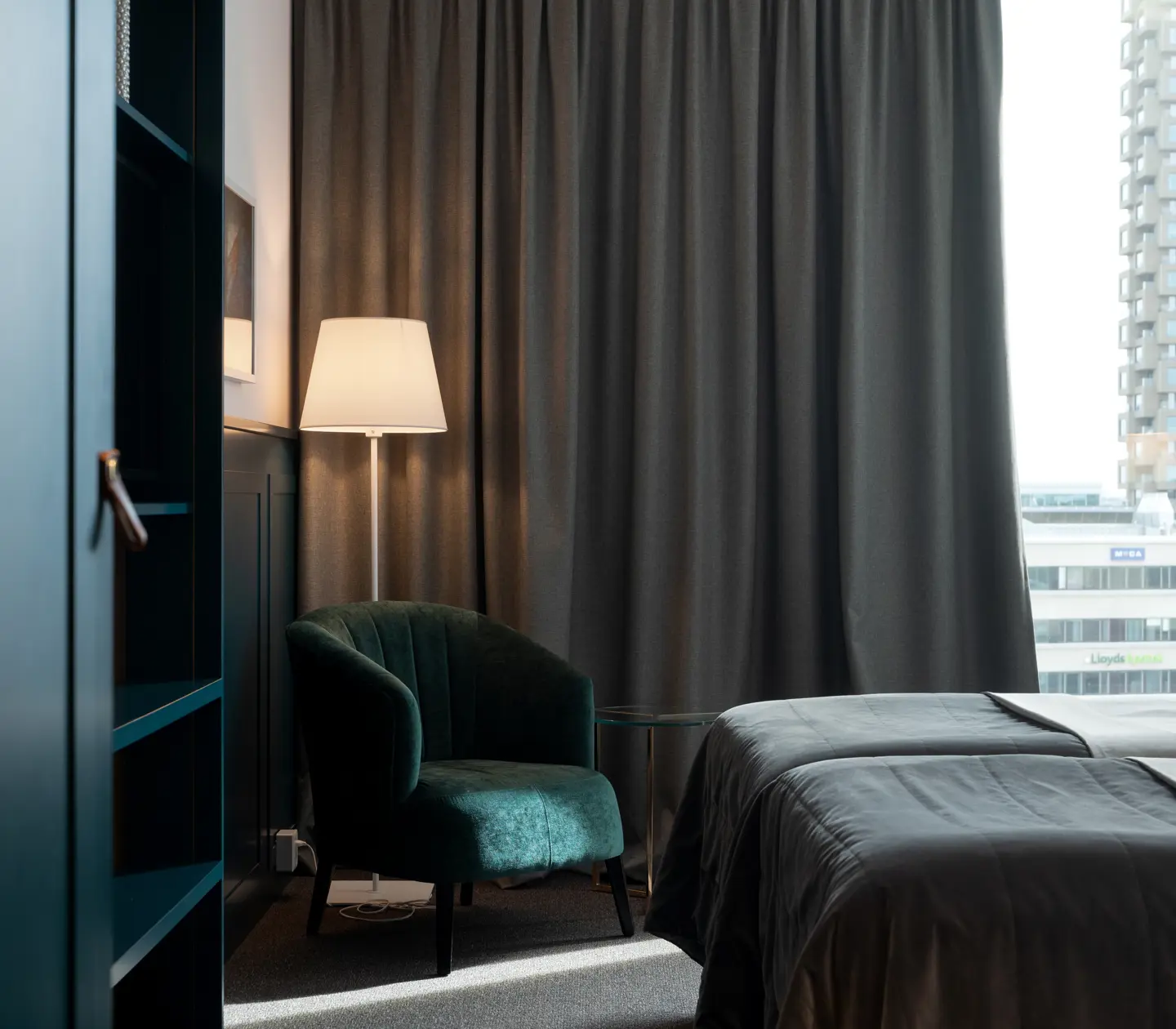 Ljust hotellrum med säng, fåtölj och stort fönster