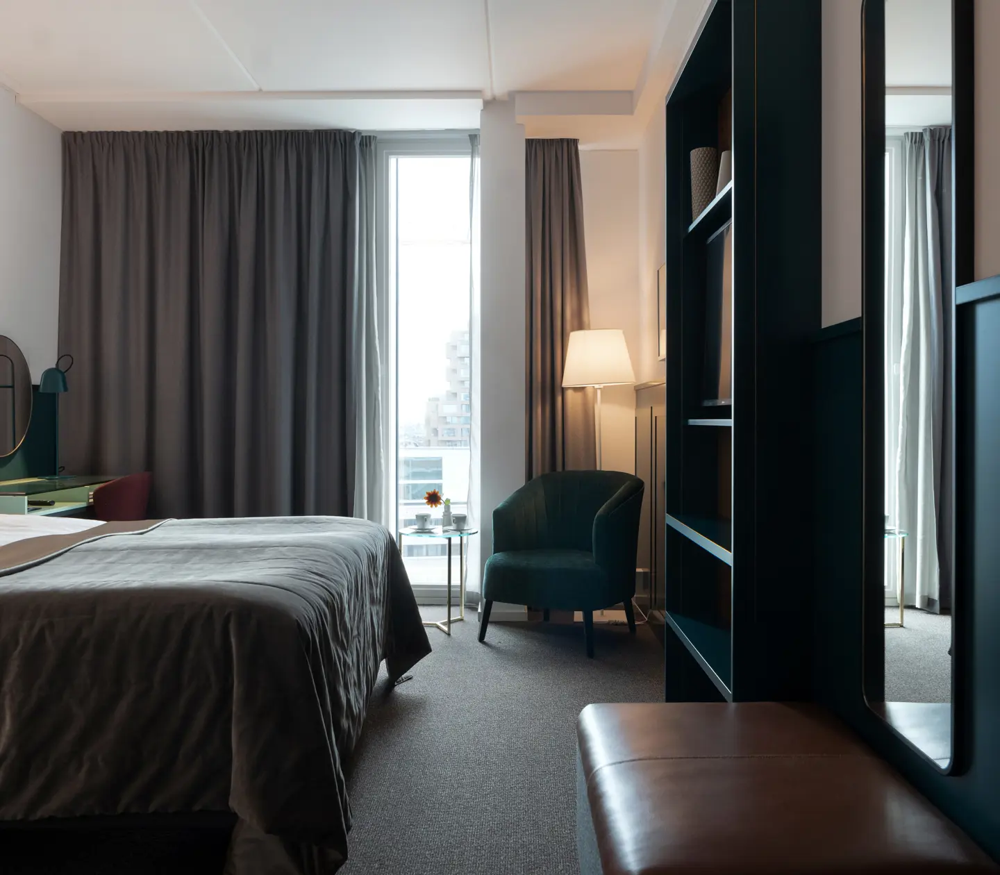 Ljust hotellrum med säng, fåtölj och bokhylla