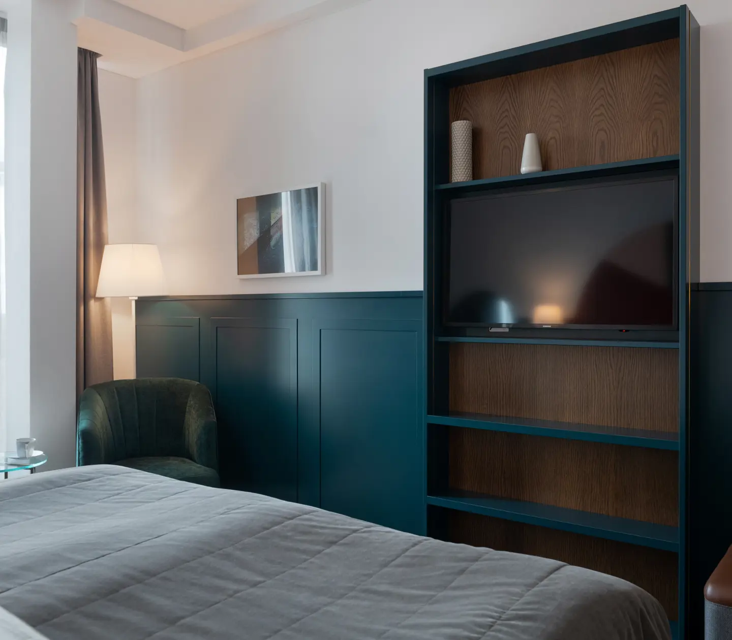 Ljust hotellrum med säng, stort fönster och bokhylla