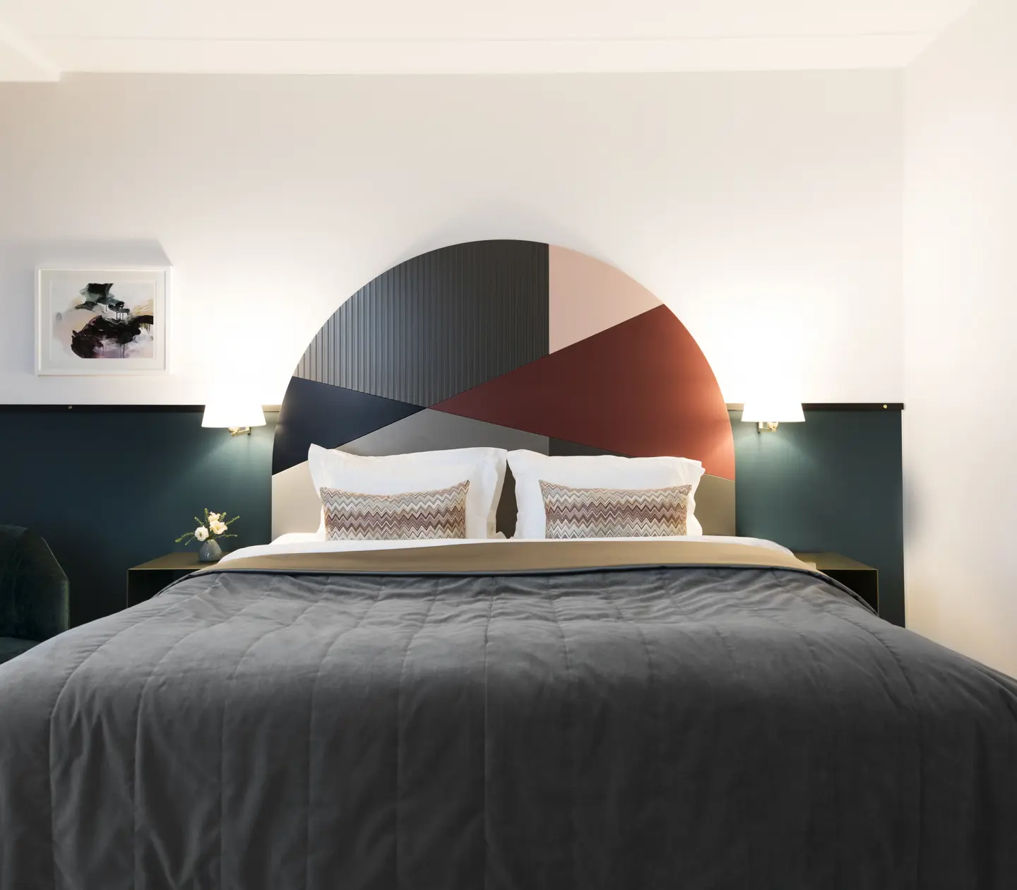 Ljust hotellrum med säng, färgglad sänggavel och sänglampor