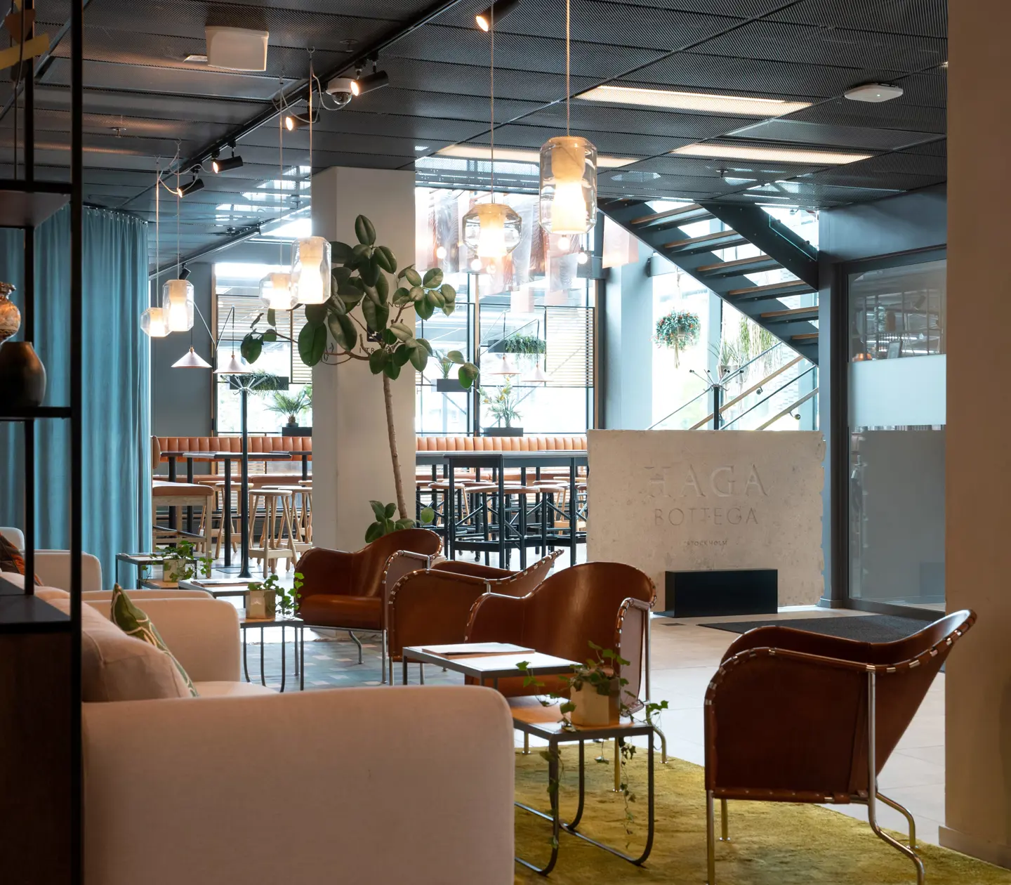 Hotellobby med skylt till "Haga Bottega", loungemöbler och växter