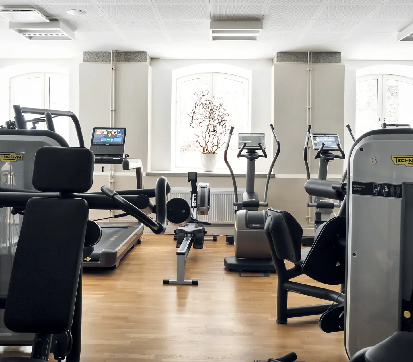 Gymmiljö med träningsmaskiner, hantlar och stora fönster