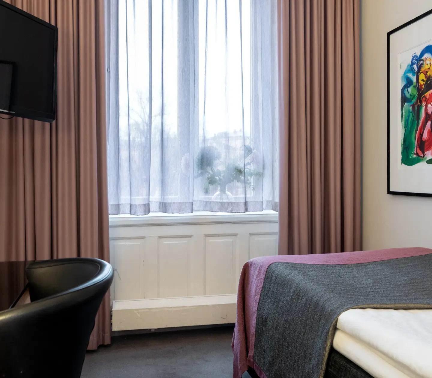 Hotellrum med enkelsäng, skrivbord, tv, tavla och stort fönster