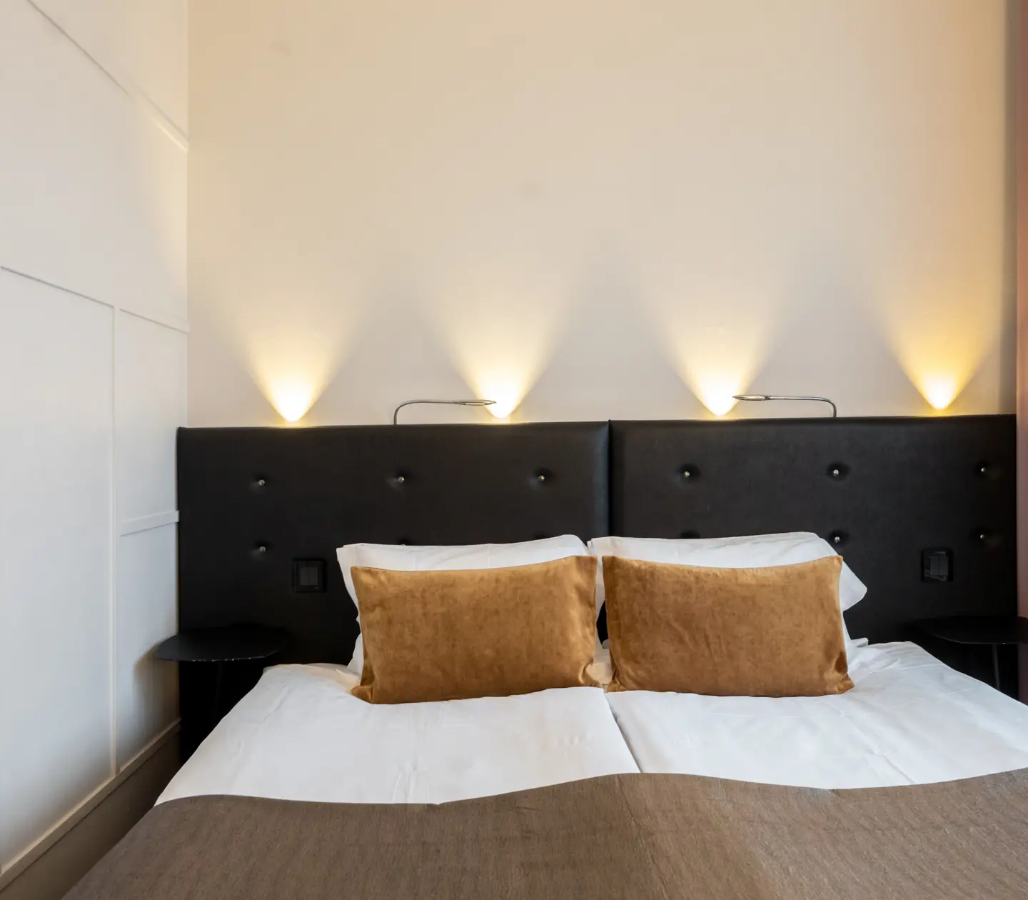 Hotellrum med fönster, dubbelsäng med svart sänggavel, lampor och gula kuddar