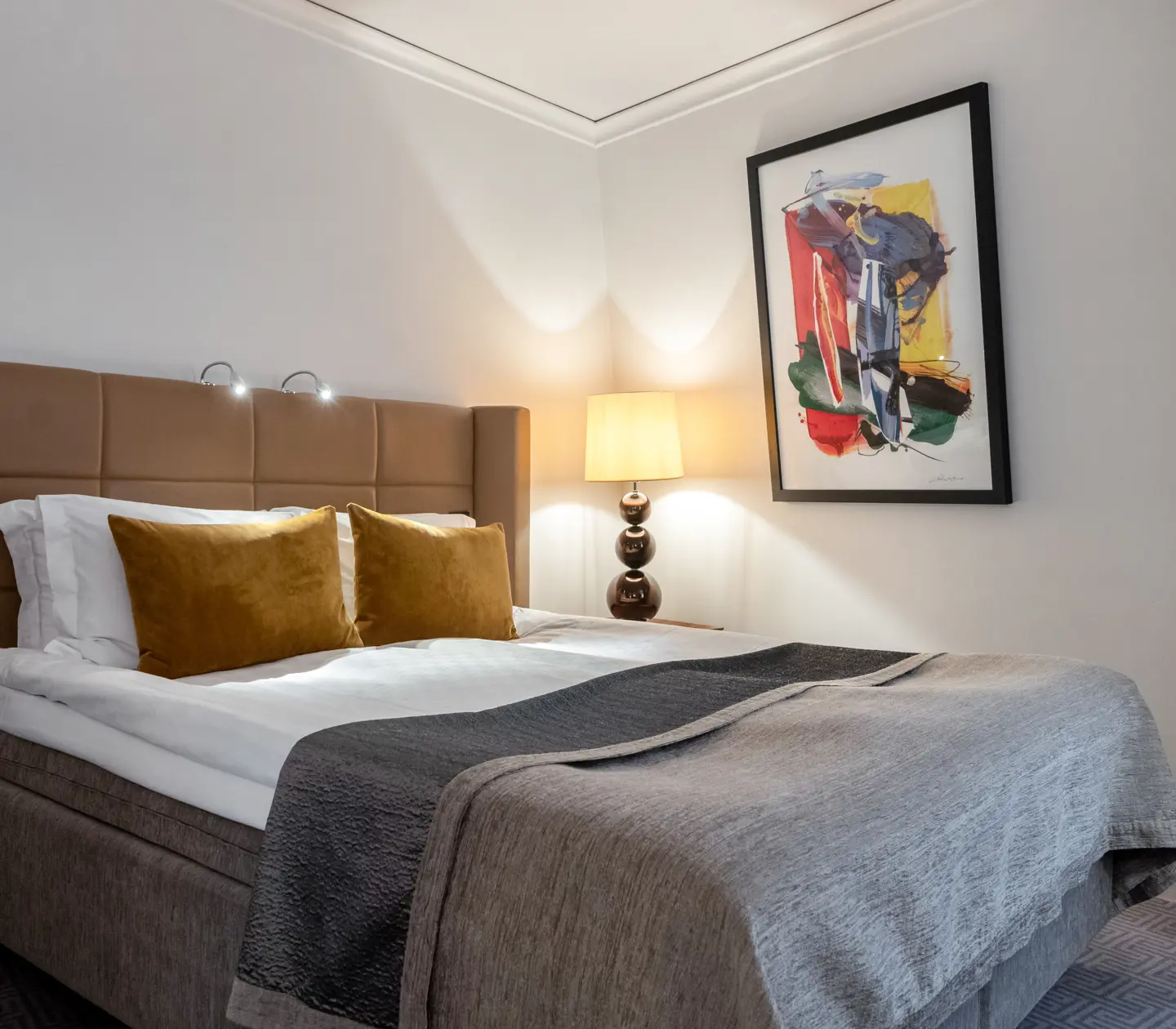 Mysigt hotellrum med dubbelsäng med gul sänggavel, lampor och tavla
