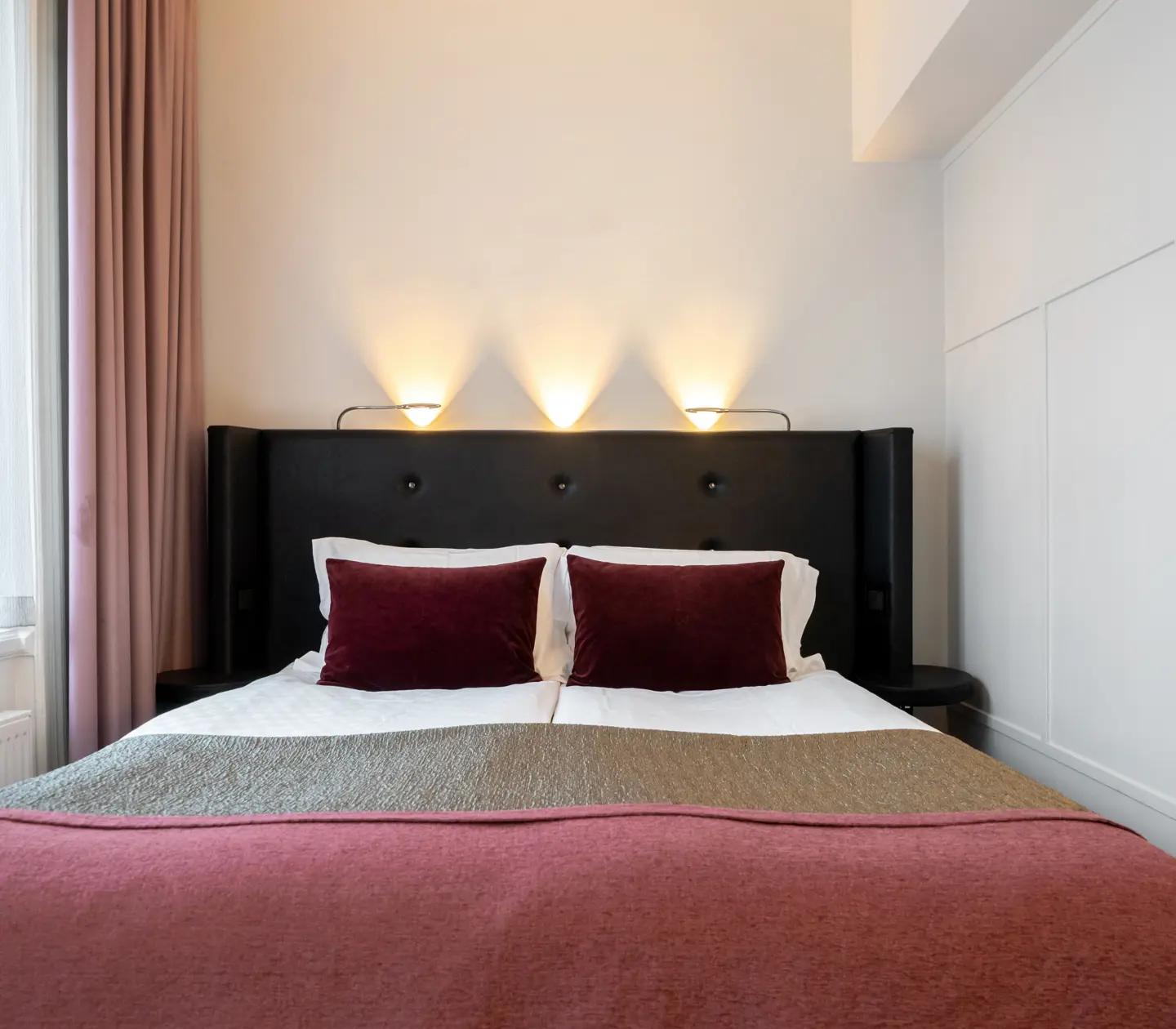 Hotellrum med dubbelsäng med svart sänggavel och rosa överkast