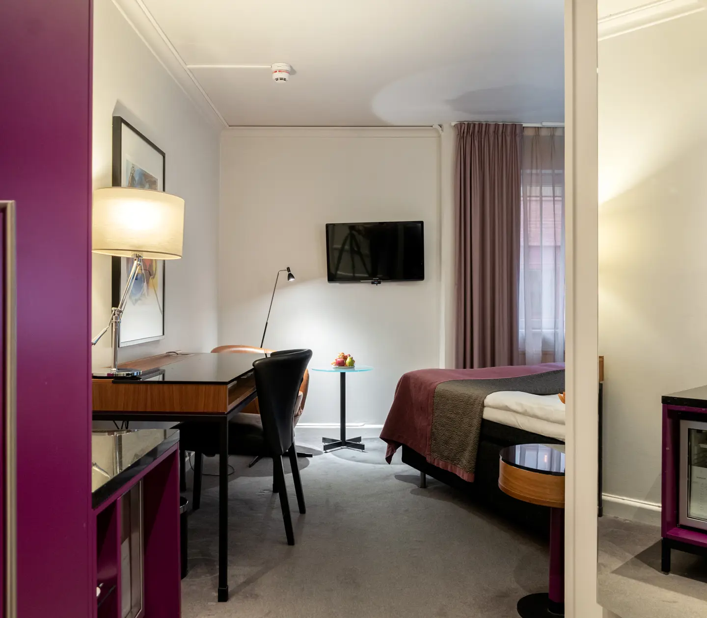 Hotellrum med dubbelsäng, skrivbord, tavla, fåtölj, tv och fönster