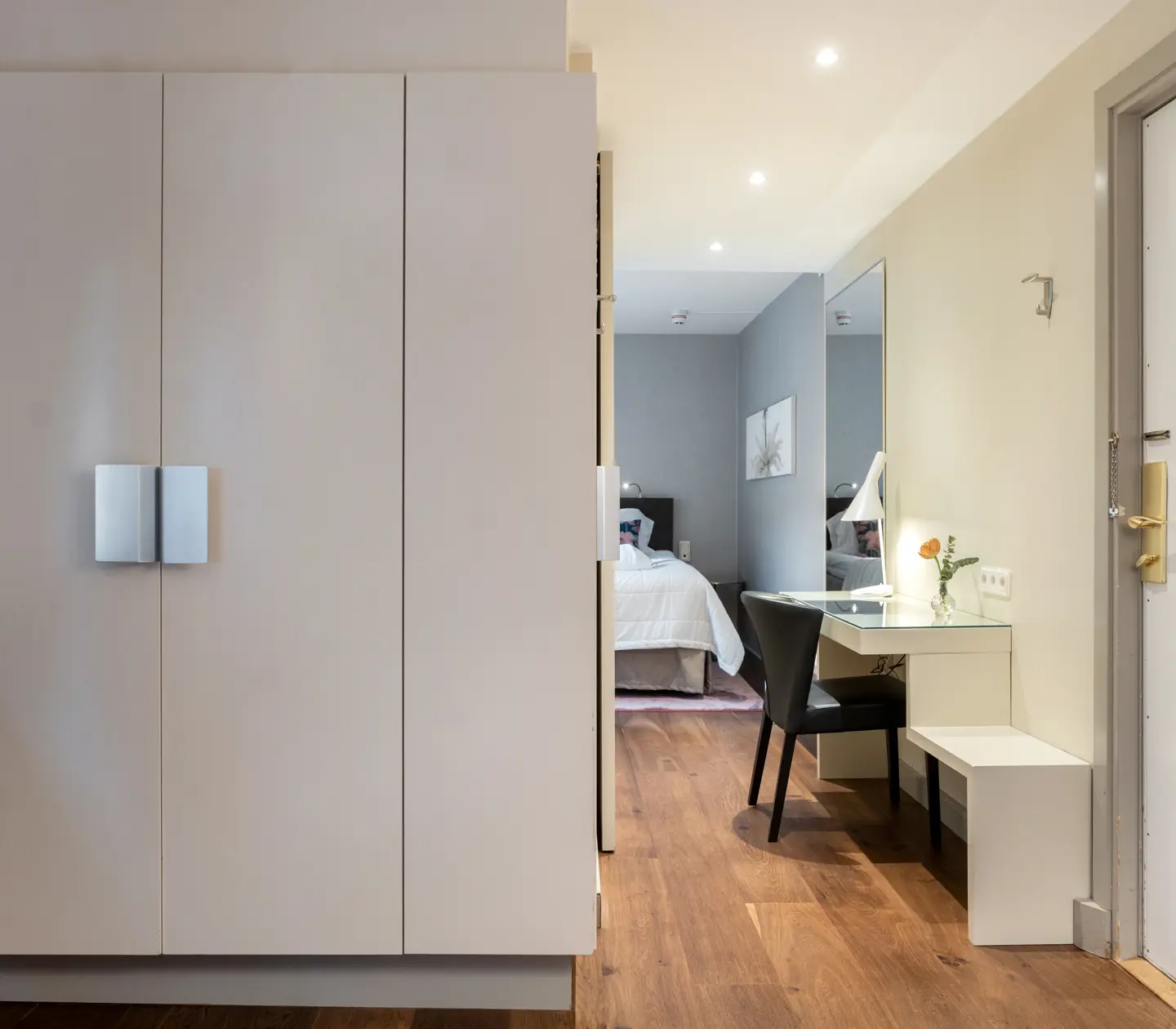 Ljust hotellrum med garderob, skrivbord, spegel och dubbelsäng