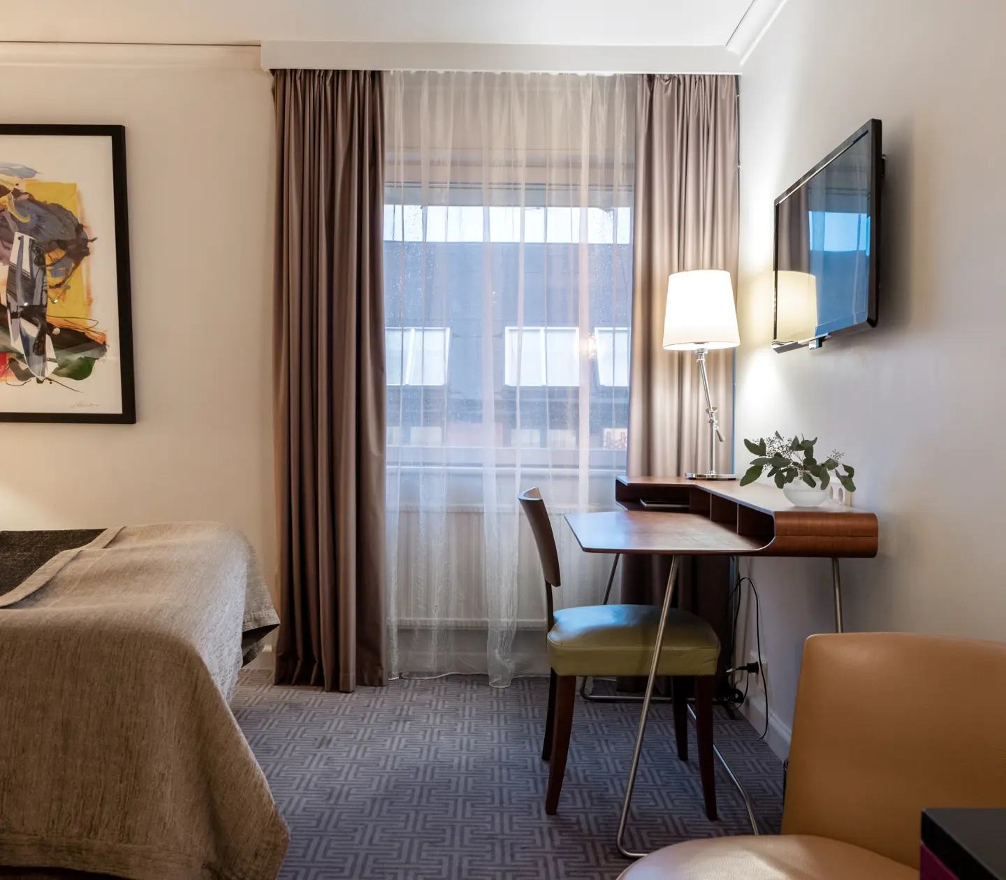 Mysig hotellsvit med dubbelsäng, skrivbord, tv, fåtölj och fönster