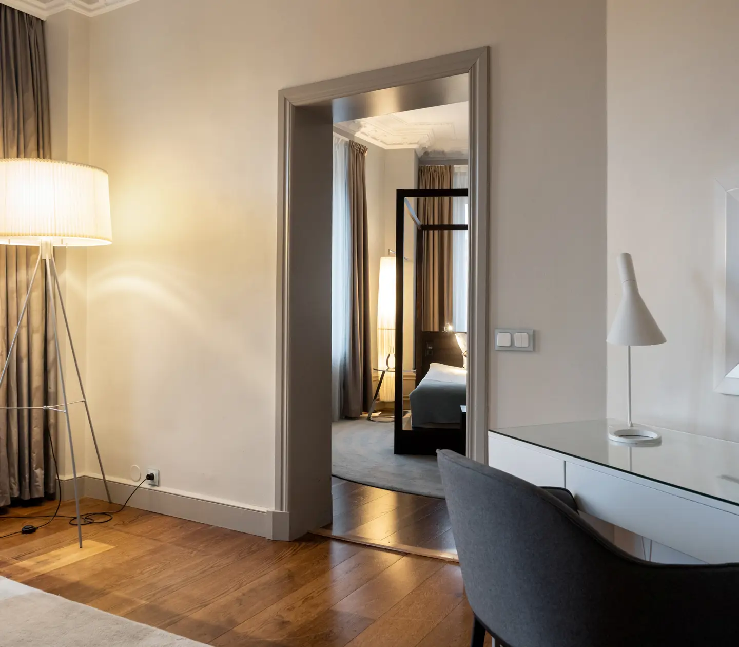Ljus hotellsvit med skrivbord, spegel, dörr in till sovrum och golvlampa
