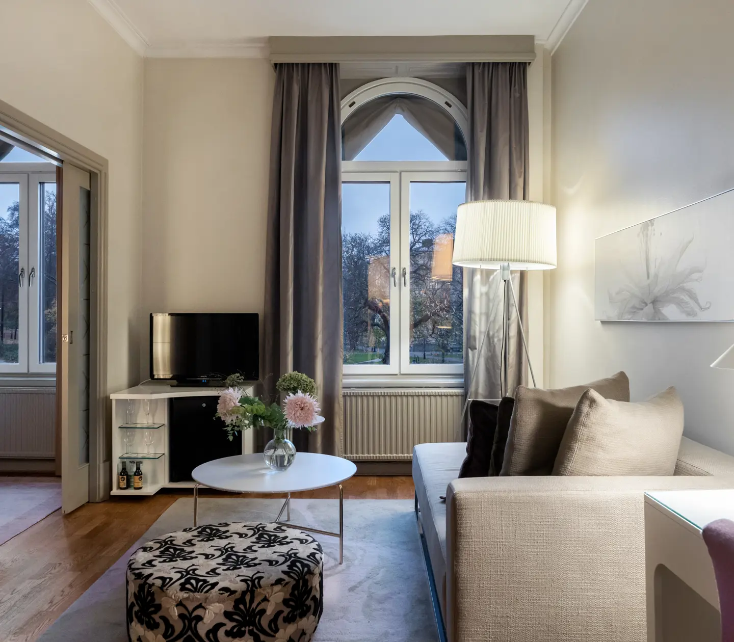 Ljust hotellrum med skrivbord, soffa, tv och stort fönster