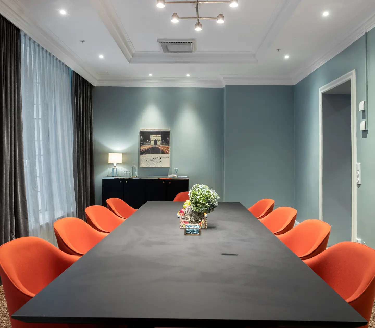 Ljusblått konferensrum med stort grått konferensbord och röda stolar omkring