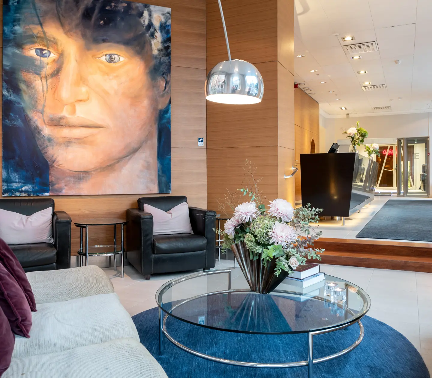 Hotellobby med stor tavla föreställande ansikte, soffor, fåtöljer och receptionsdisk