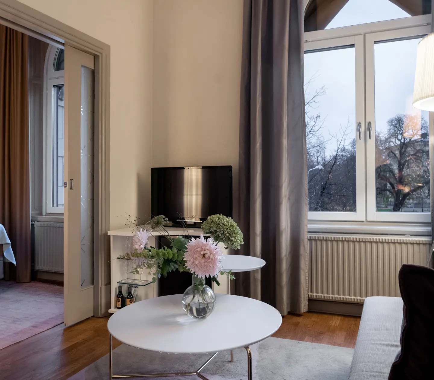 Mysig hotellsvit med dörr in till sovrum, soffa, bukett och stort fönster