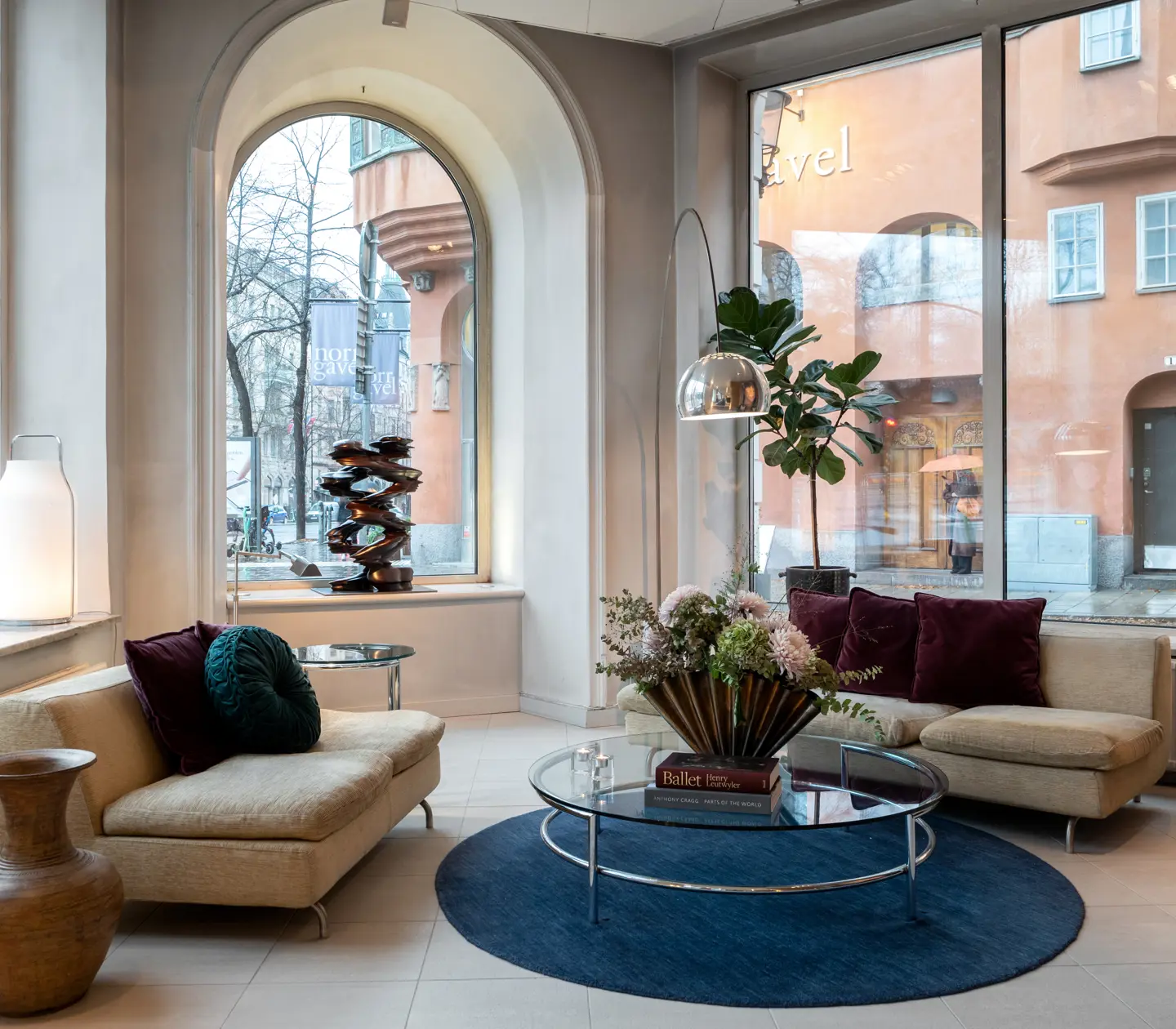 Ljus hotellobby med soffor, bord, bukett och stora fönster med mycket ljusinsläpp