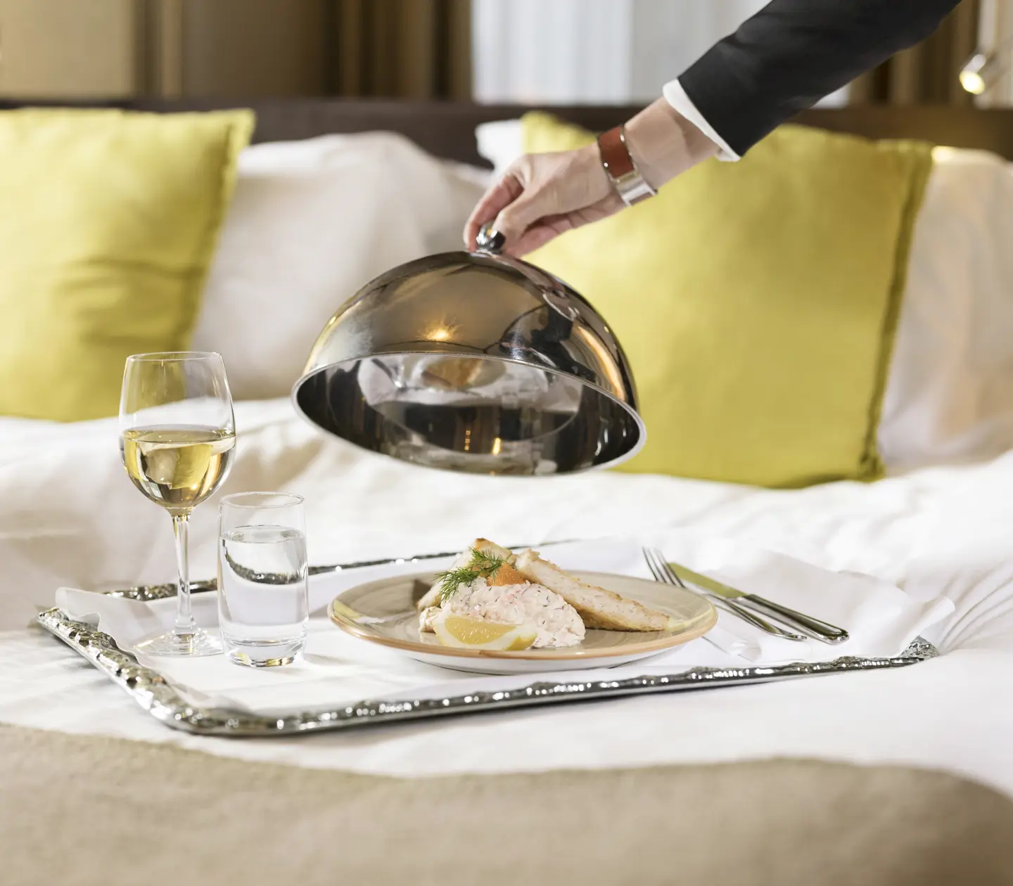 Roomservice serverat på hotellsäng i form av Toast Skagen och ett glas vitt vin