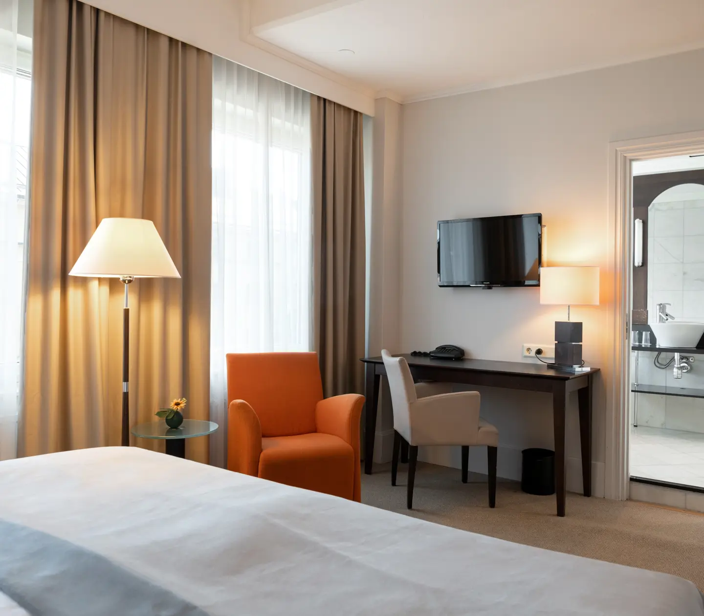 Skrivbord, golvlampa, tv och ingång till badrum i hotellrum