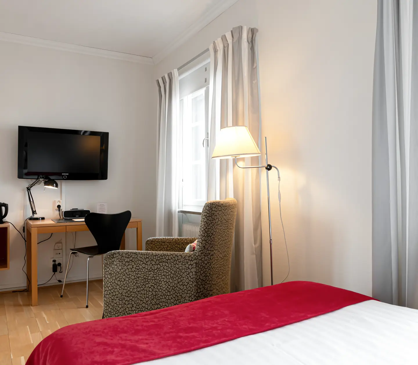 Ljust hotellrum med skrivbord, fåtölj och tv
