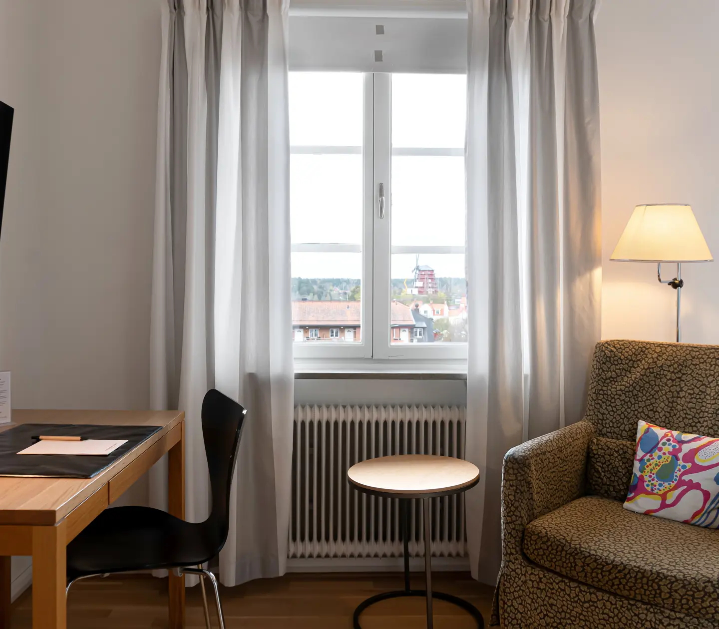 Ljust hotellrum med skrivbord, fåtölj och fönster