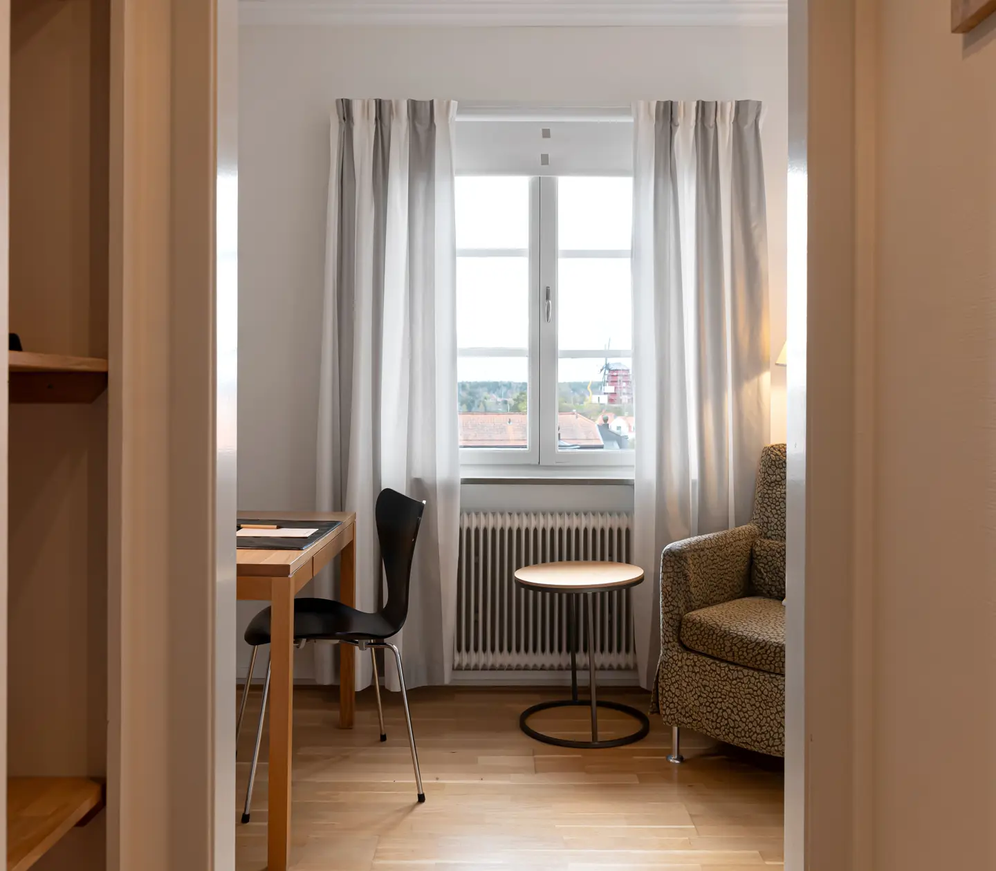 Ljust hotellrum med skrivbord, fåtölj och fönster