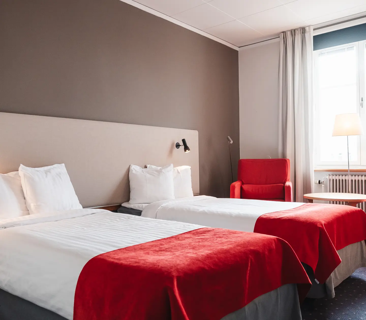 Mysigt hotellrum med sängar, röda fåtöljer och fönster