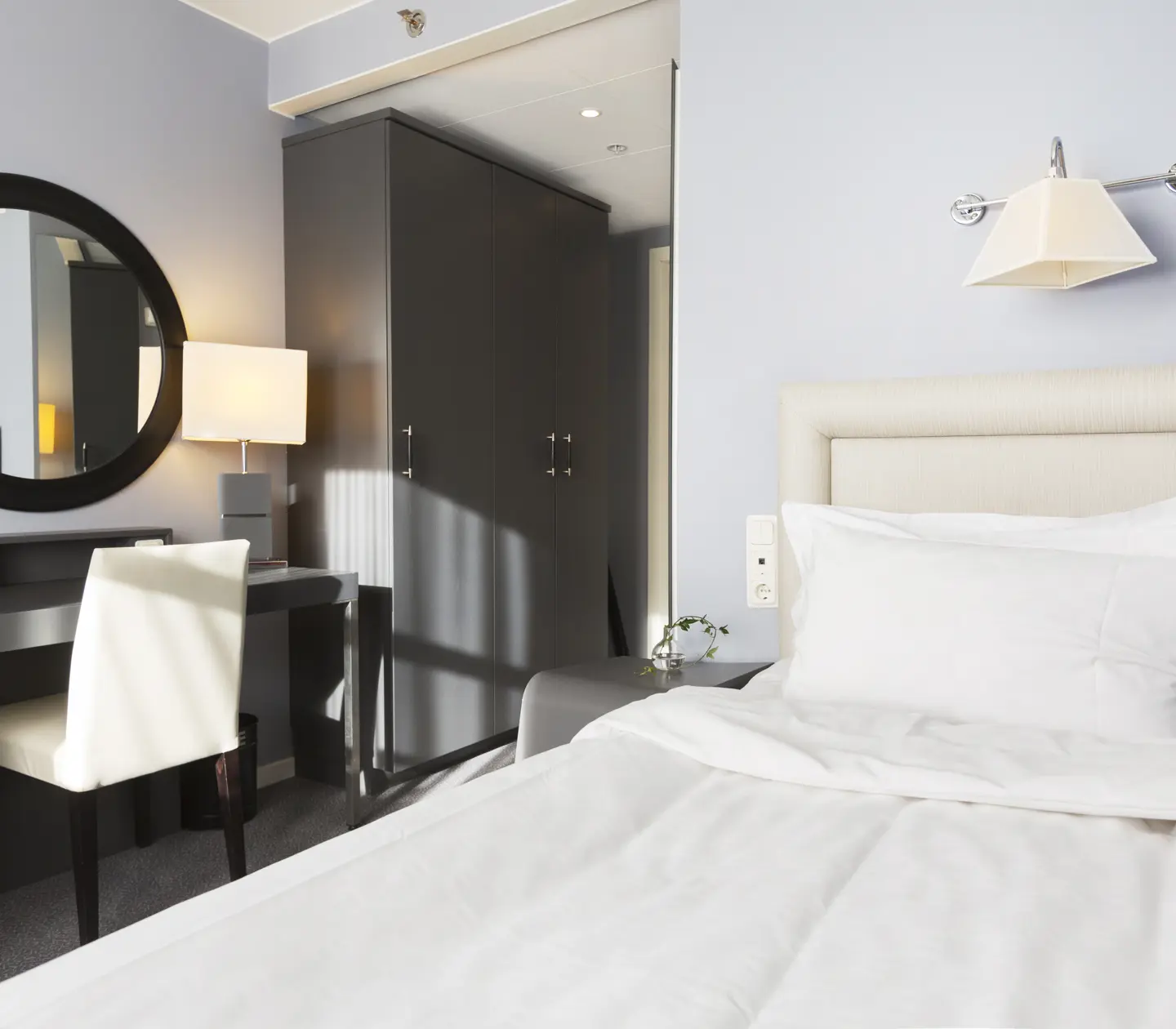 Litet hotellrum med säng, skrivbord och spegel