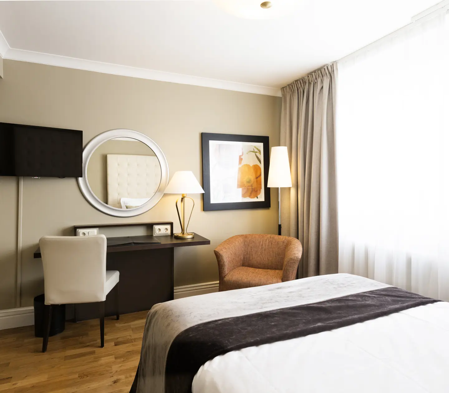 Litet hotellrum med säng, skrivbord och fåtölj