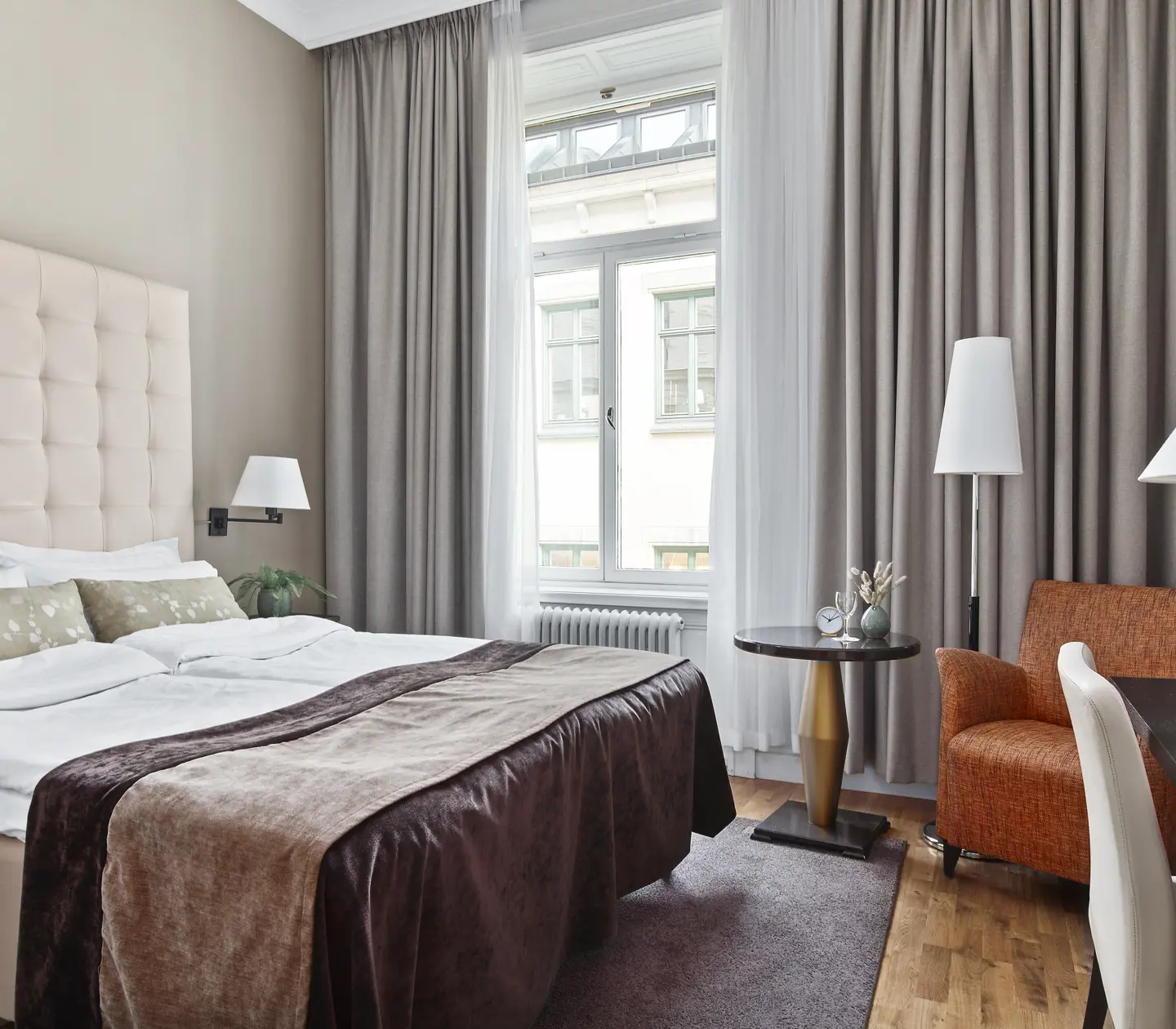 Ljust hotellrum med säng, vit sänggavel och fåtölj