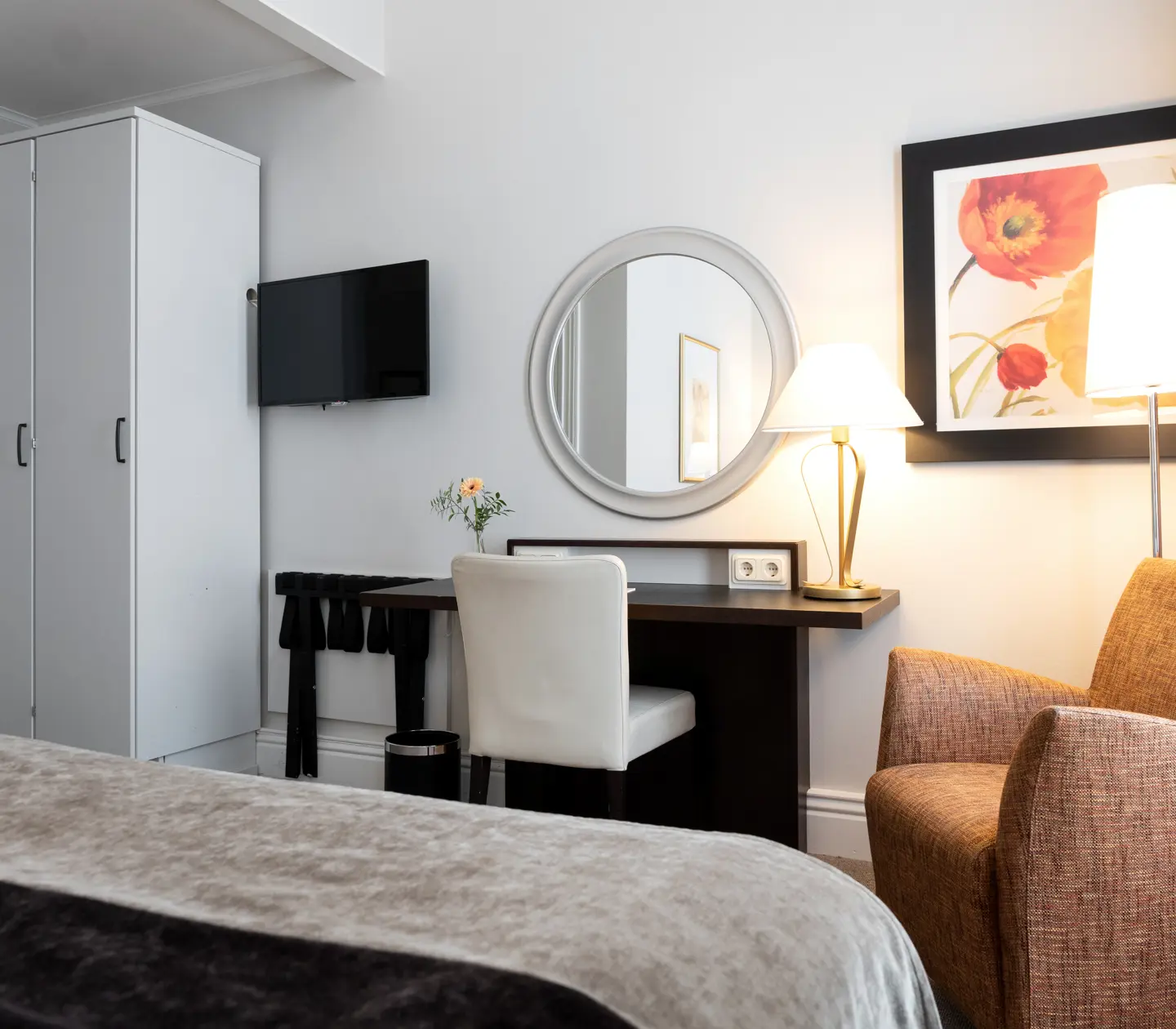 Ljust hotellrum med garderob, skrivbord och fåtölj