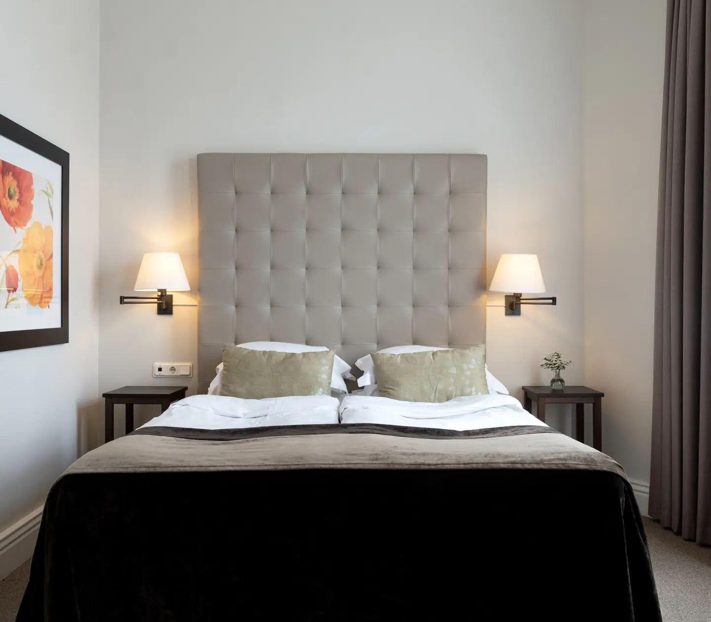 Ljust hotellrum med säng, grå sänggavel och tavla