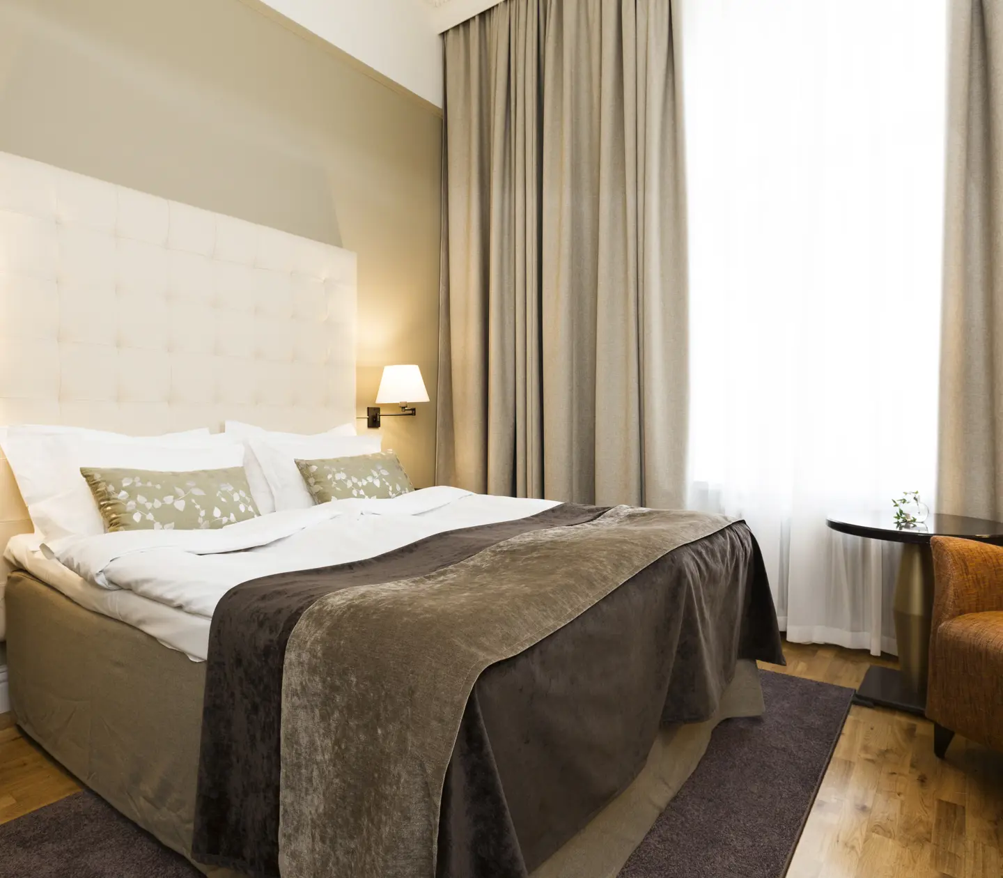 Ljust hotellrum med säng, vit sänggavel och fåtölj