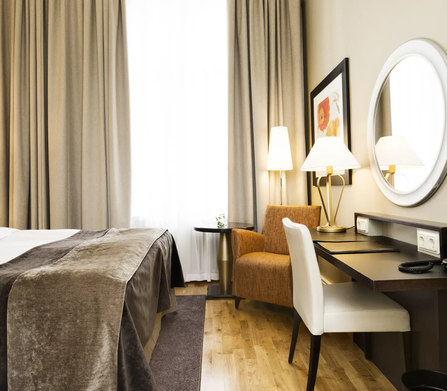 Ljust hotellrum med säng, skrivbord och fåtölj
