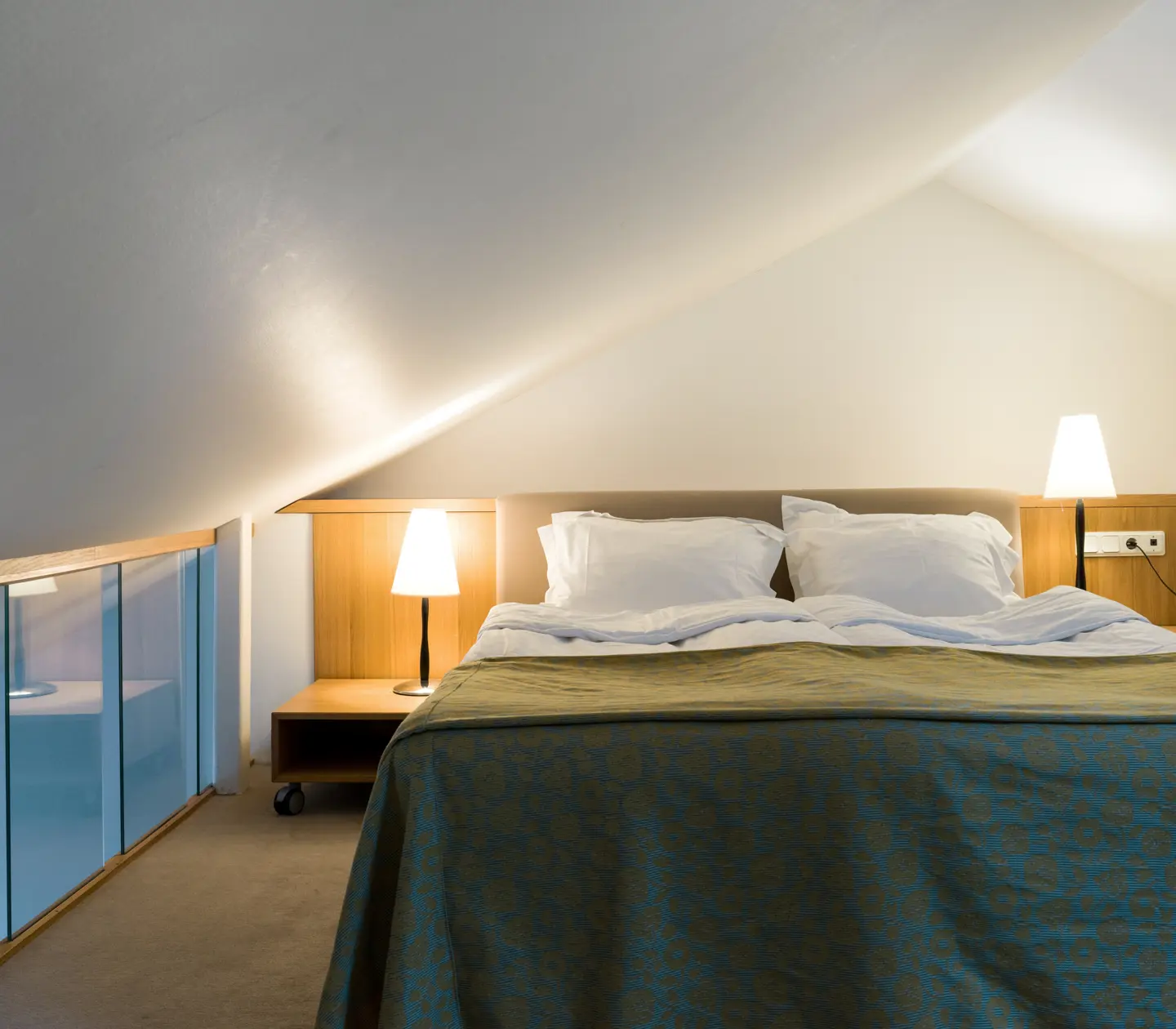 Ljust hotellrum med säng, glasräcke och sänglampor