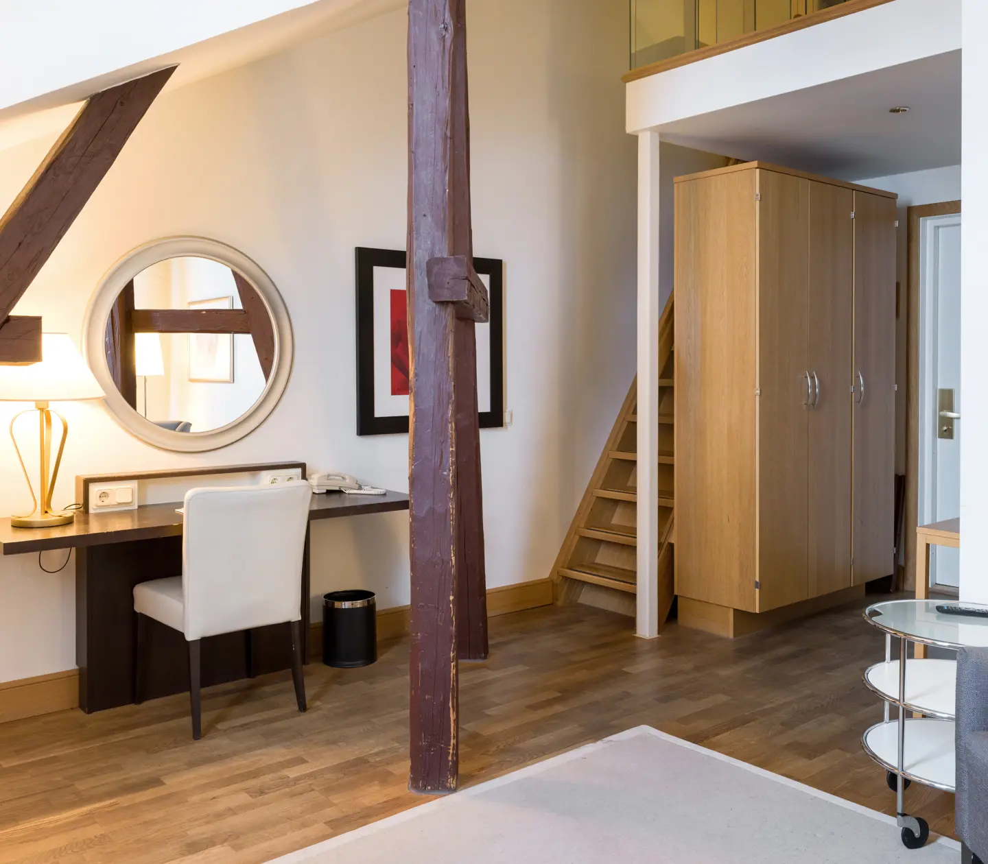Ljust hotellrum med garderob, skrivbord och trapp till sovloft