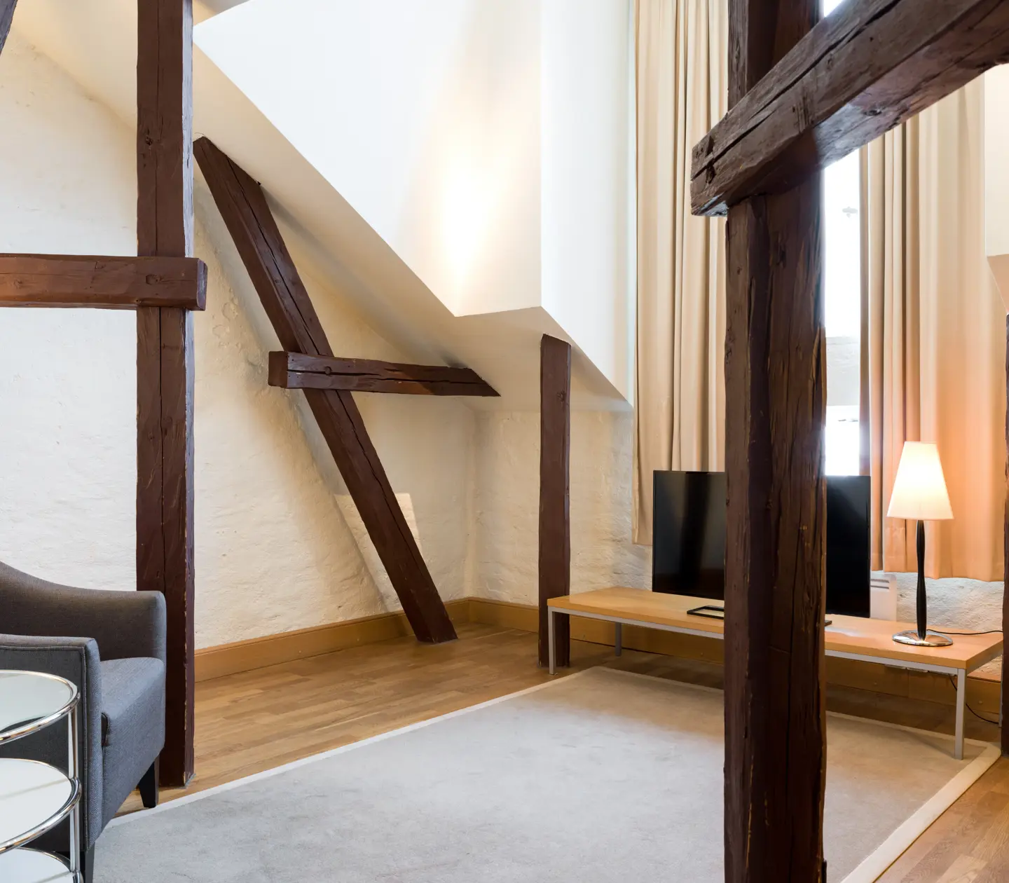 Ljust hotellrum med träbalkar från tak, fåtölj och tv