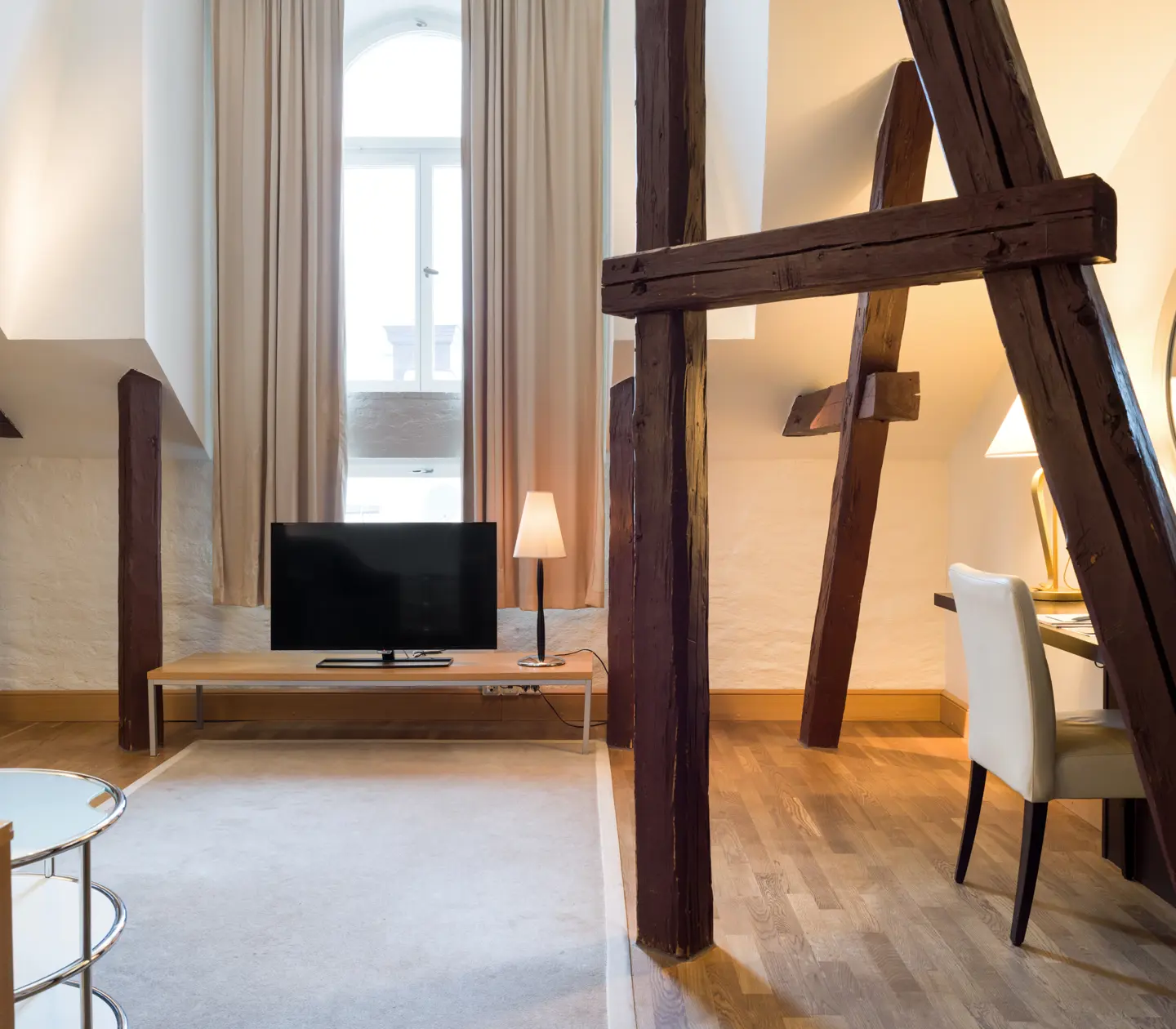 Ljust hotellrum med träbalkar från tak, skrivbord och tv