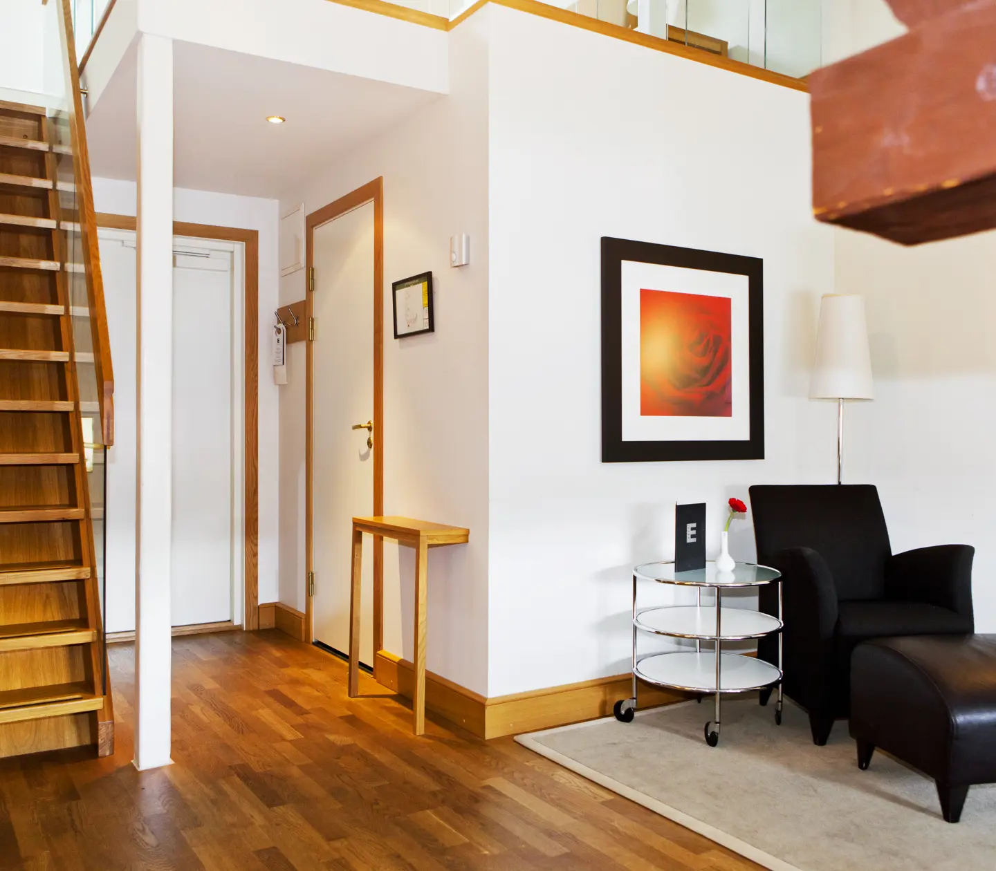 Ljust hotellrum med fåtölj, tavla och trapp till sovloft