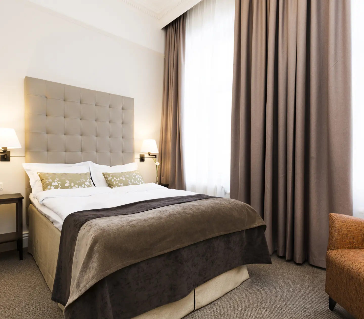 Ljust hotellrum med säng, grå sänggavel och fåtölj