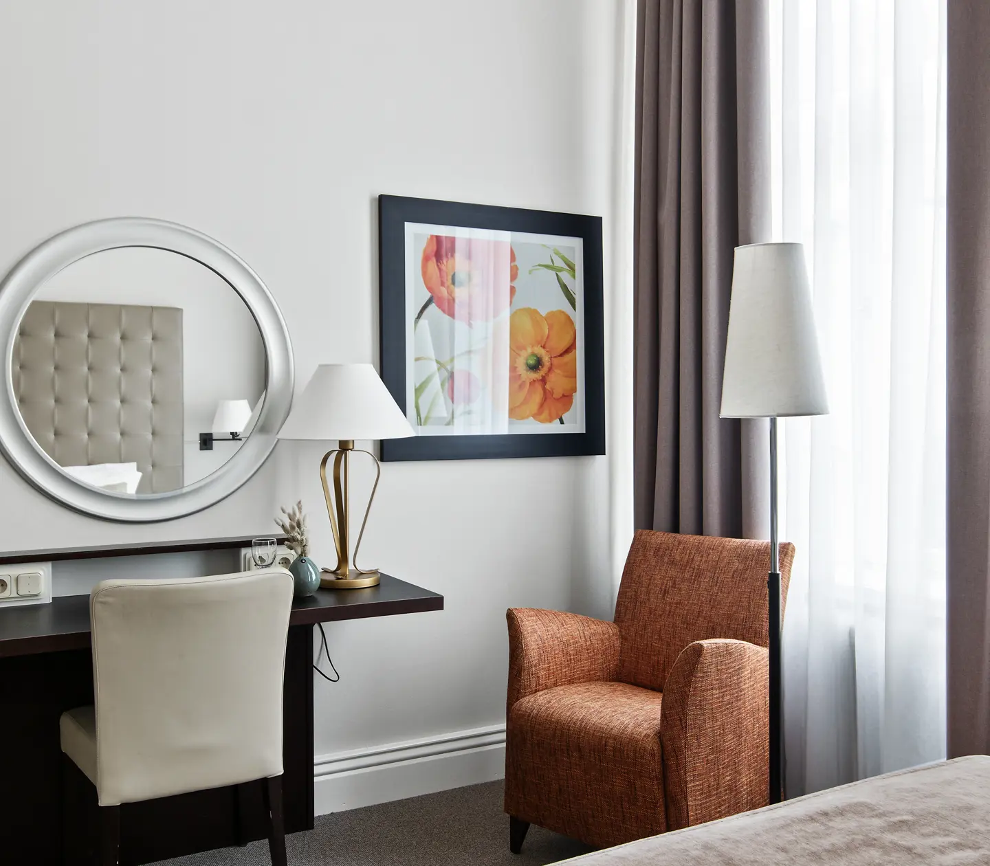 Ljust hotellrum med skrivbord, fåtölj och rund spegel