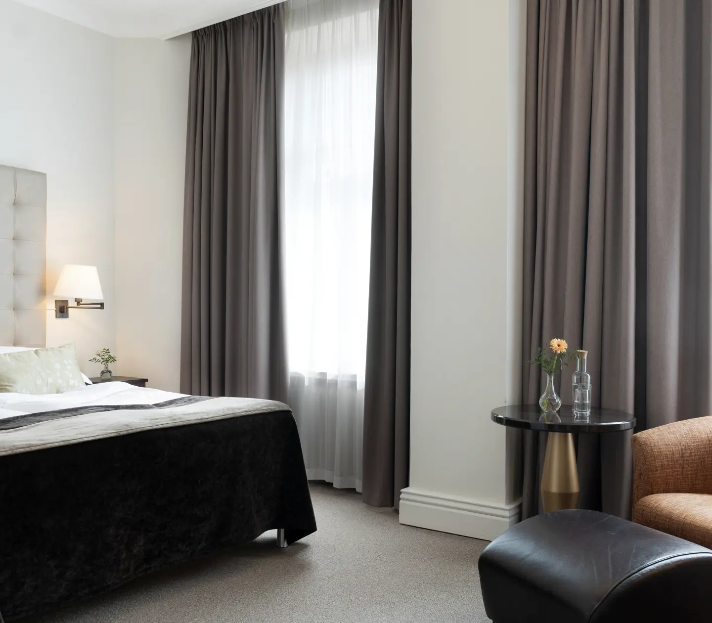 Ljust hotellrum med säng, vit sänggavel och fåtöljer
