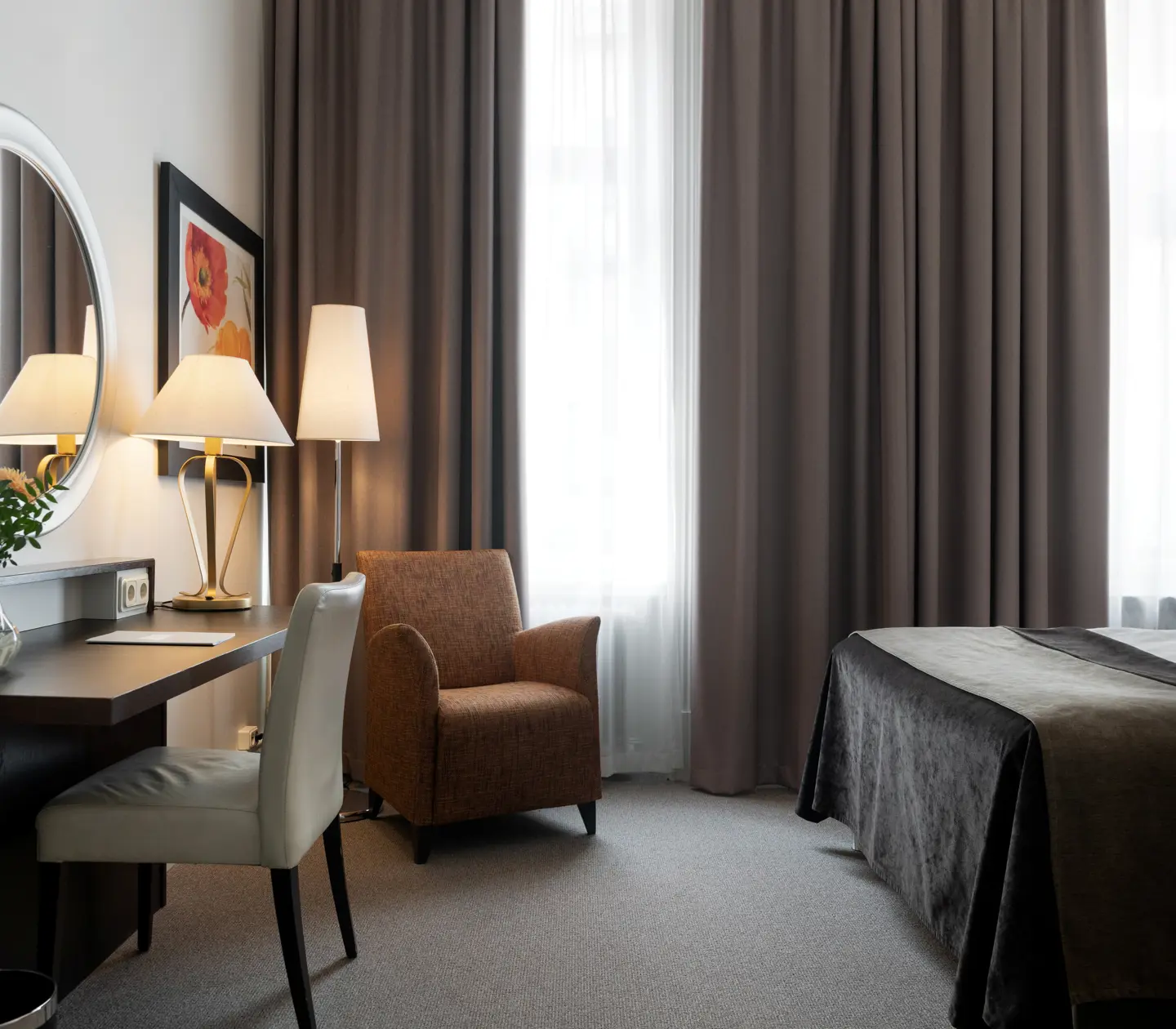Ljust hotellrum med säng, skrivbord och fåtölj