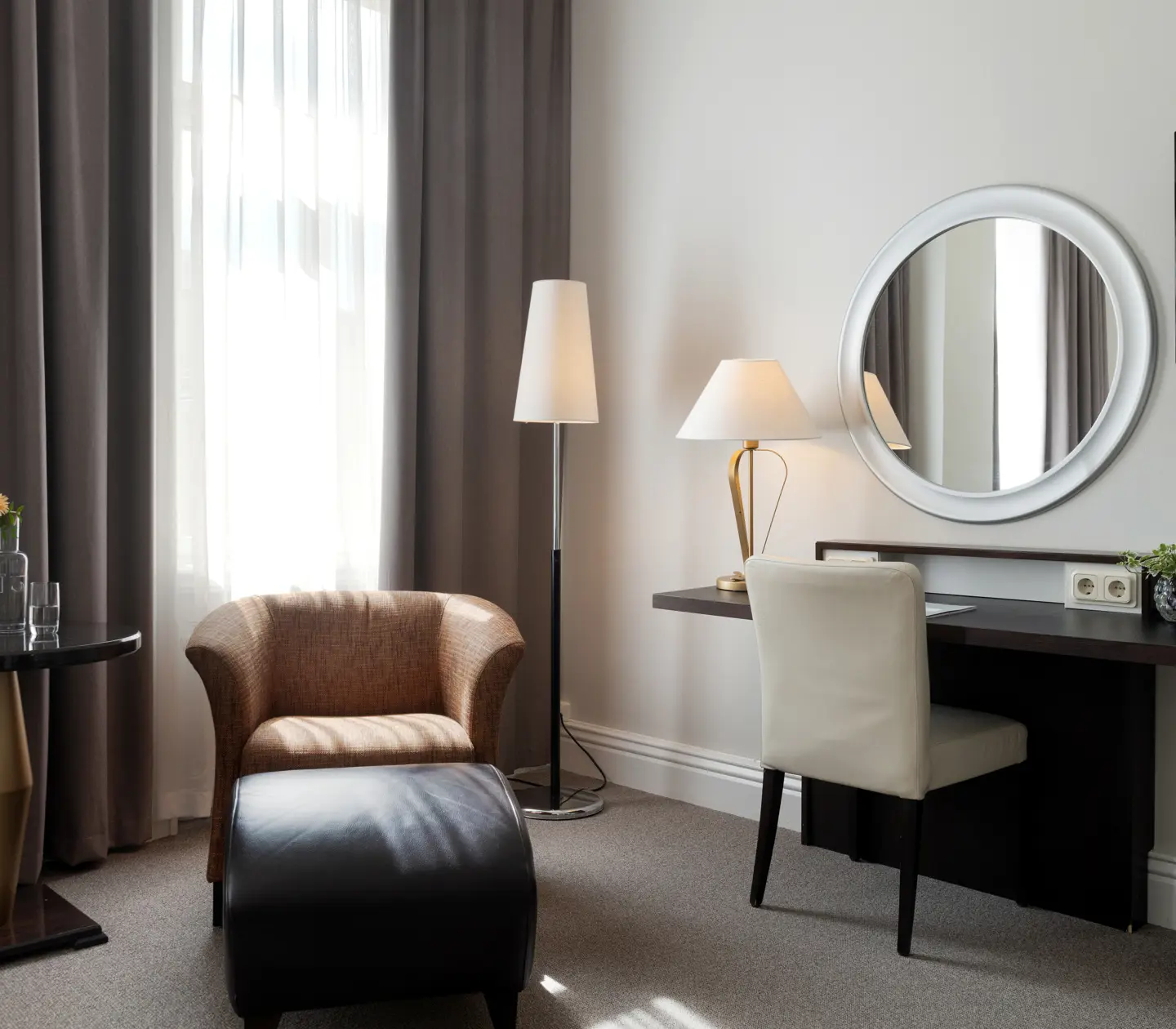 Ljust hotellrum med rund spegel, skrivbord och fåtölj