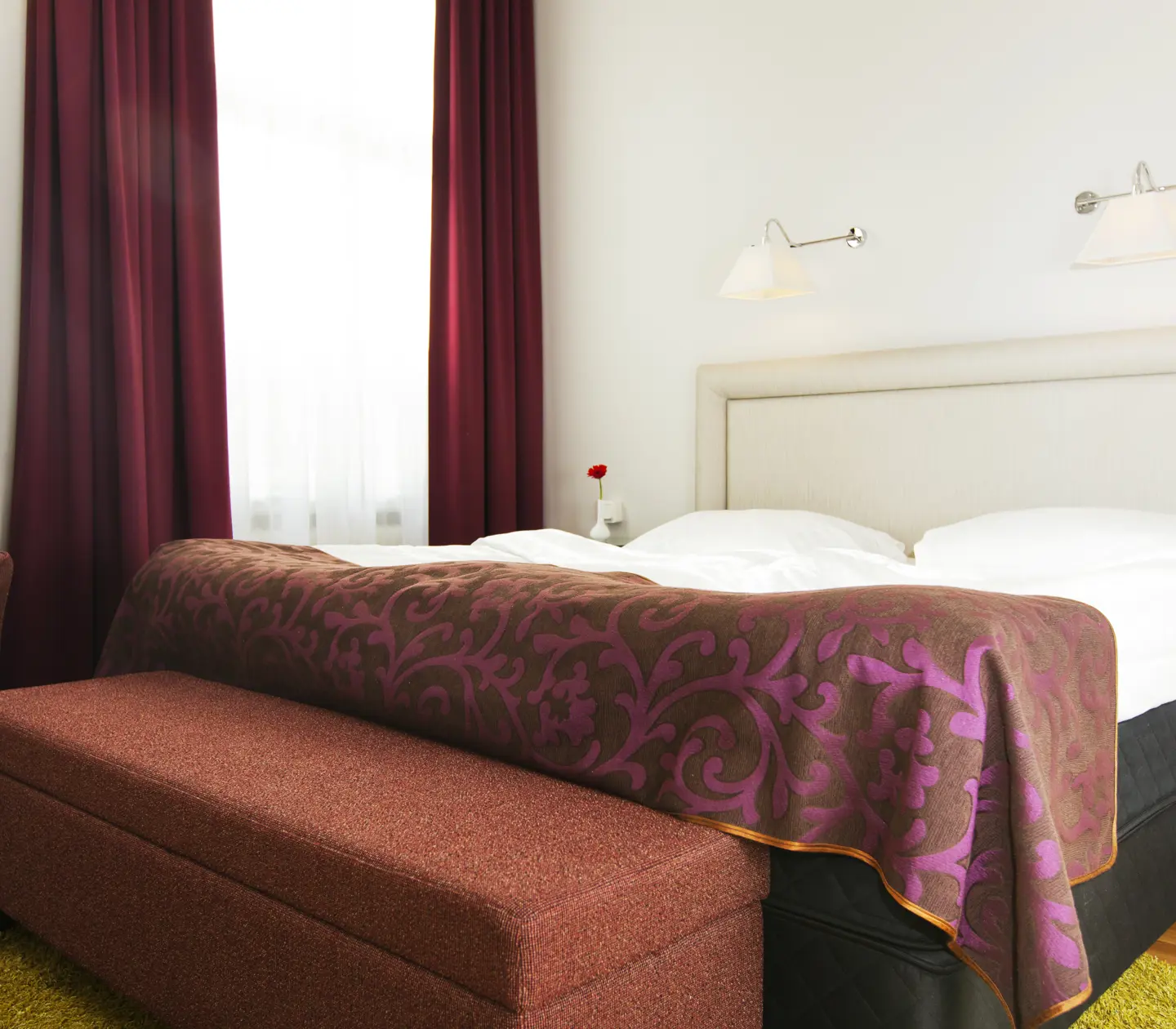 Ljust hotellrum med säng, vit sänggavel och fåtölj