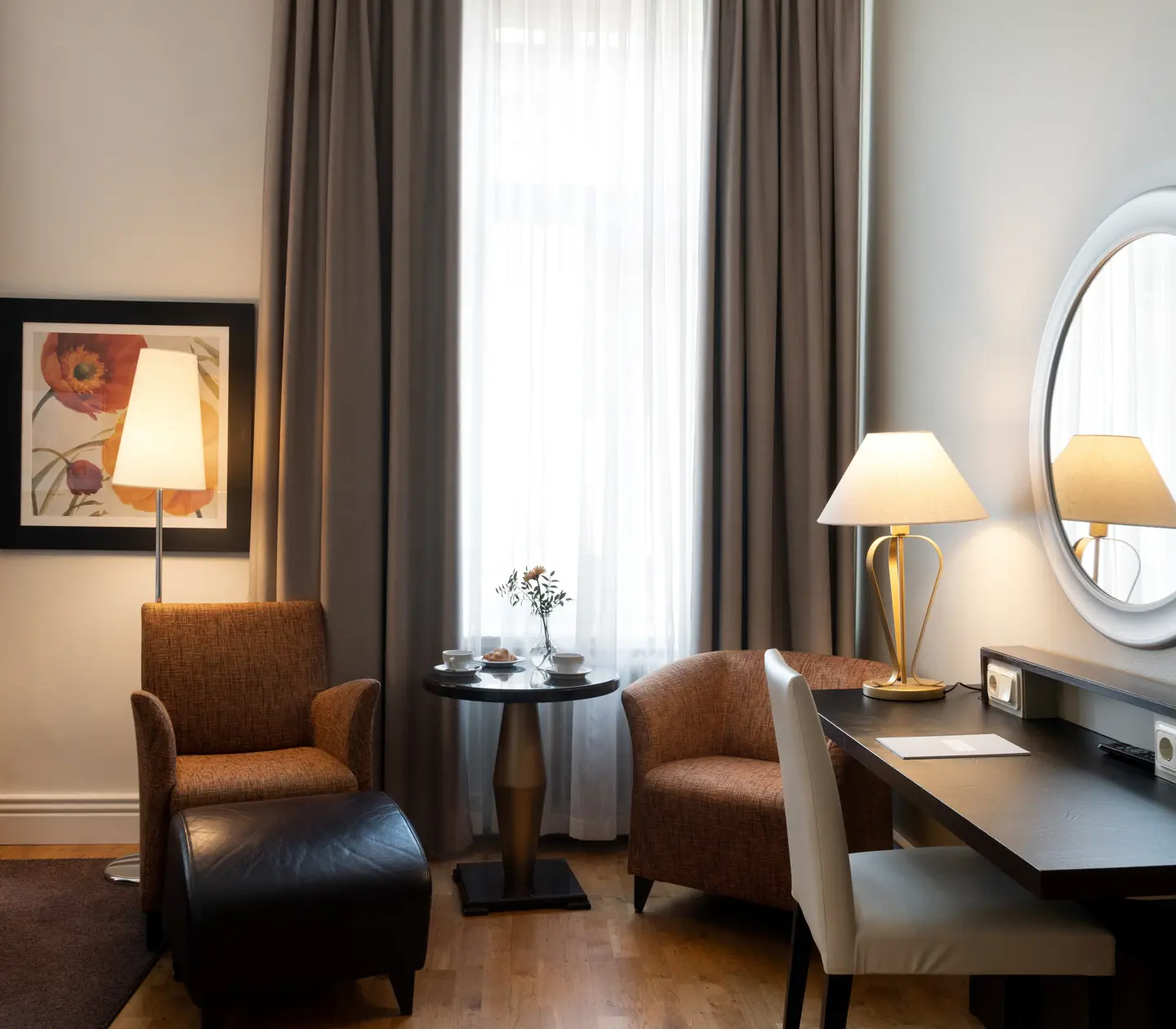 Ljust hotellrum med stort fönster, skrivbord och fåtöljer