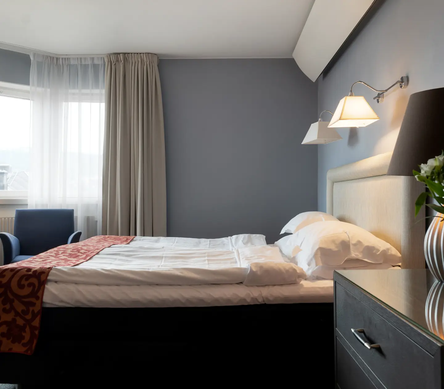 Ljust hotellrum med säng, vit sänggavel och fåtölj