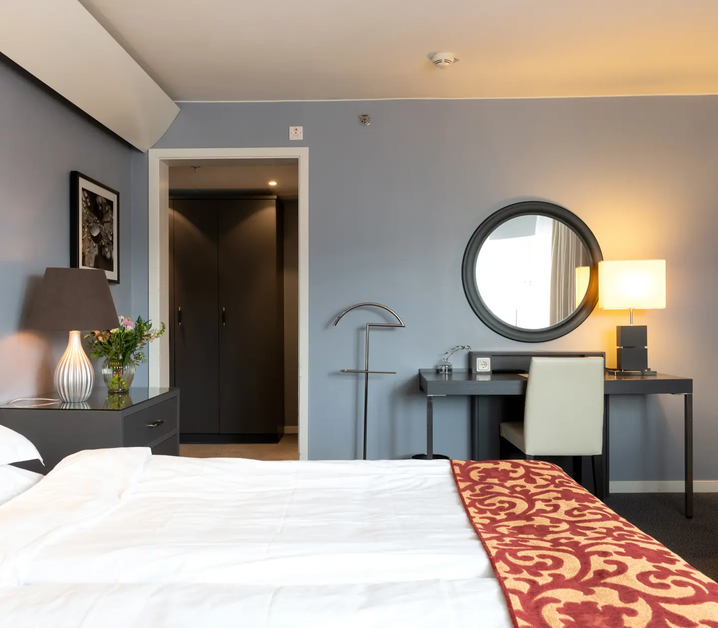 Ljust hotellrum med säng, skrivbord och rund spegel